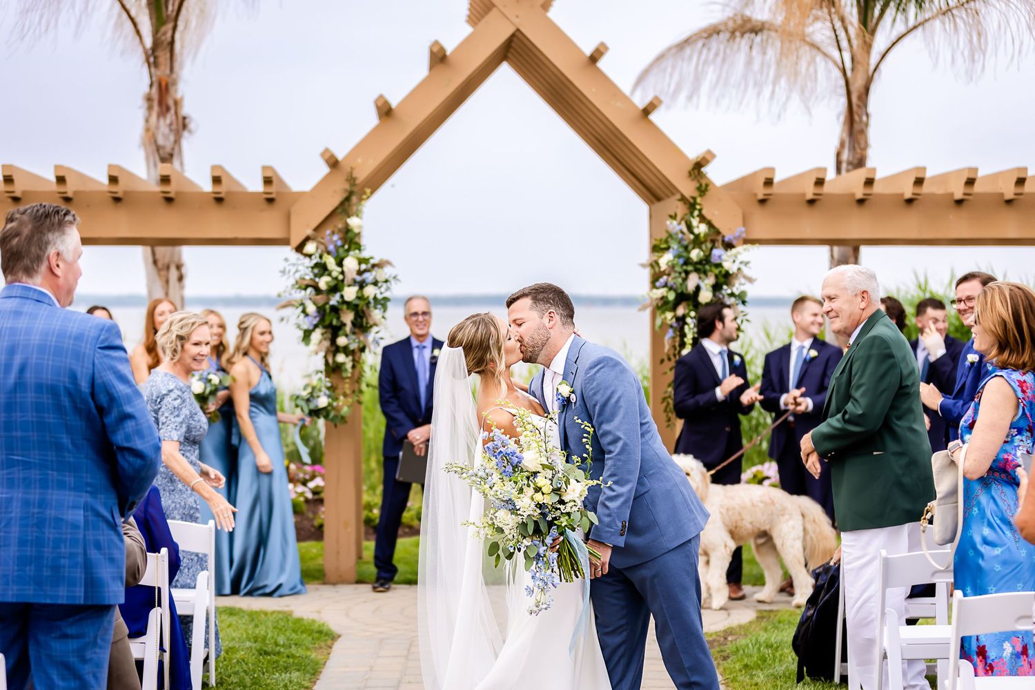 Wedding celebration under wooden pergola with guests mingling during outdoor daytime reception.
