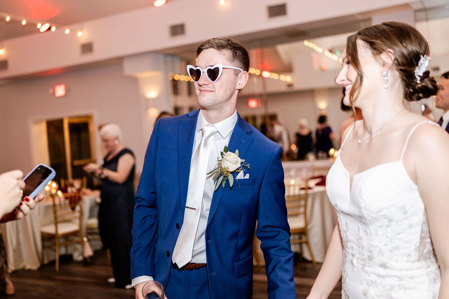 Wedding celebration with guests in formal attire dancing and laughing in a bright reception venue.