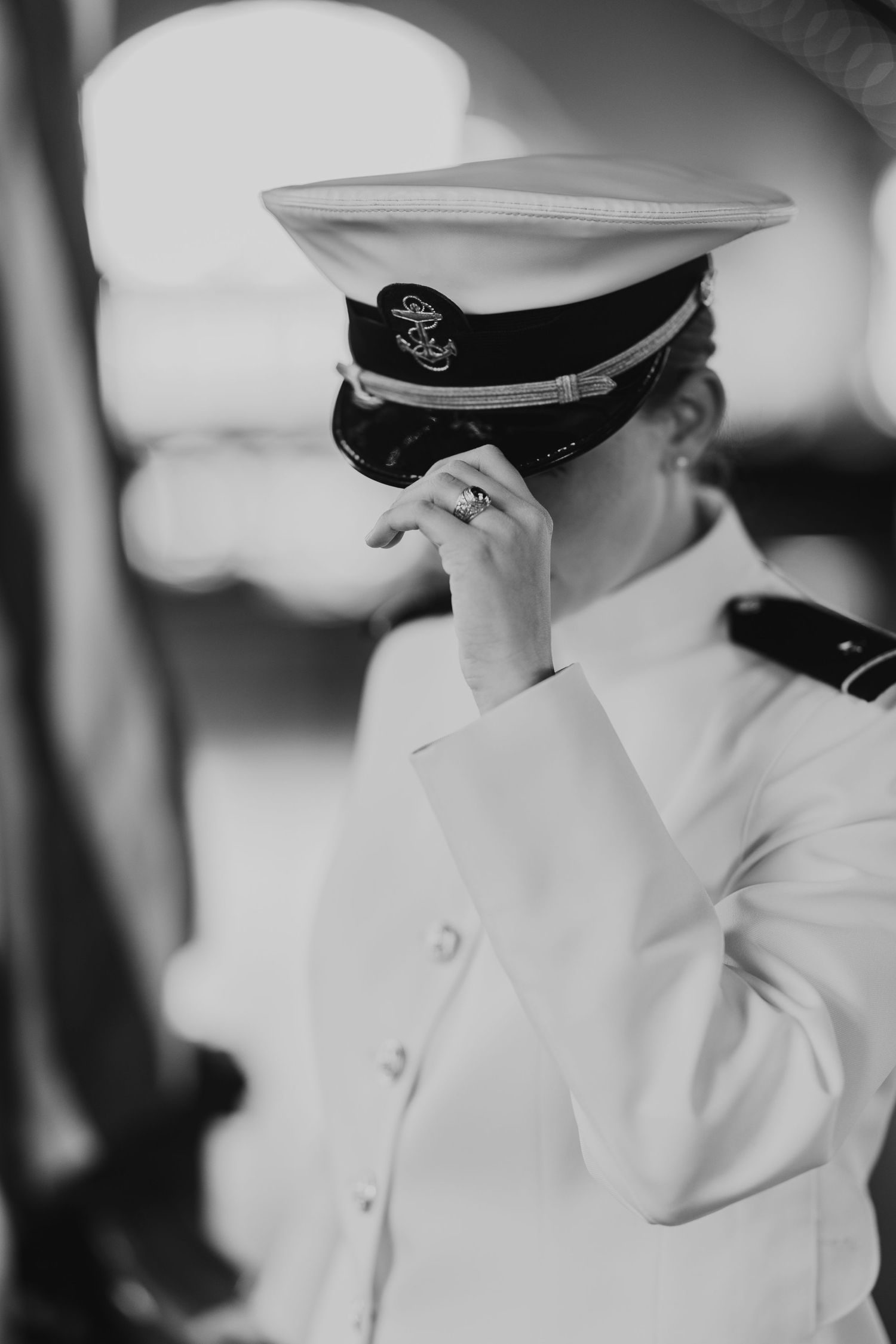 A military officer in dress whites and peaked cap stands in a contemplative black and white portrait pose.