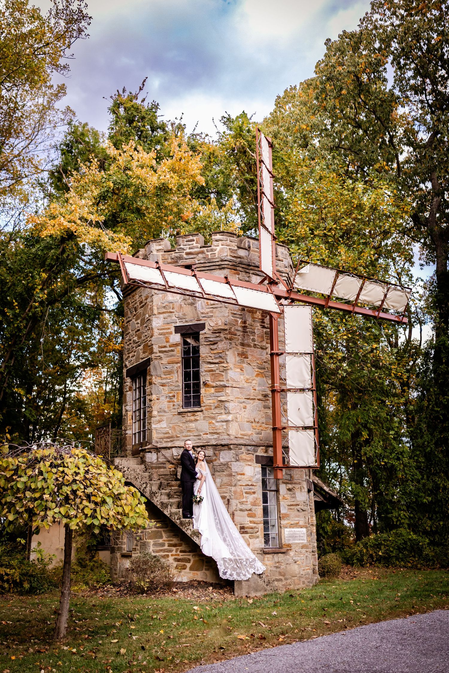 A flowing white wedding dress hangs from an abandoned stone building in a wooded area during autumn.