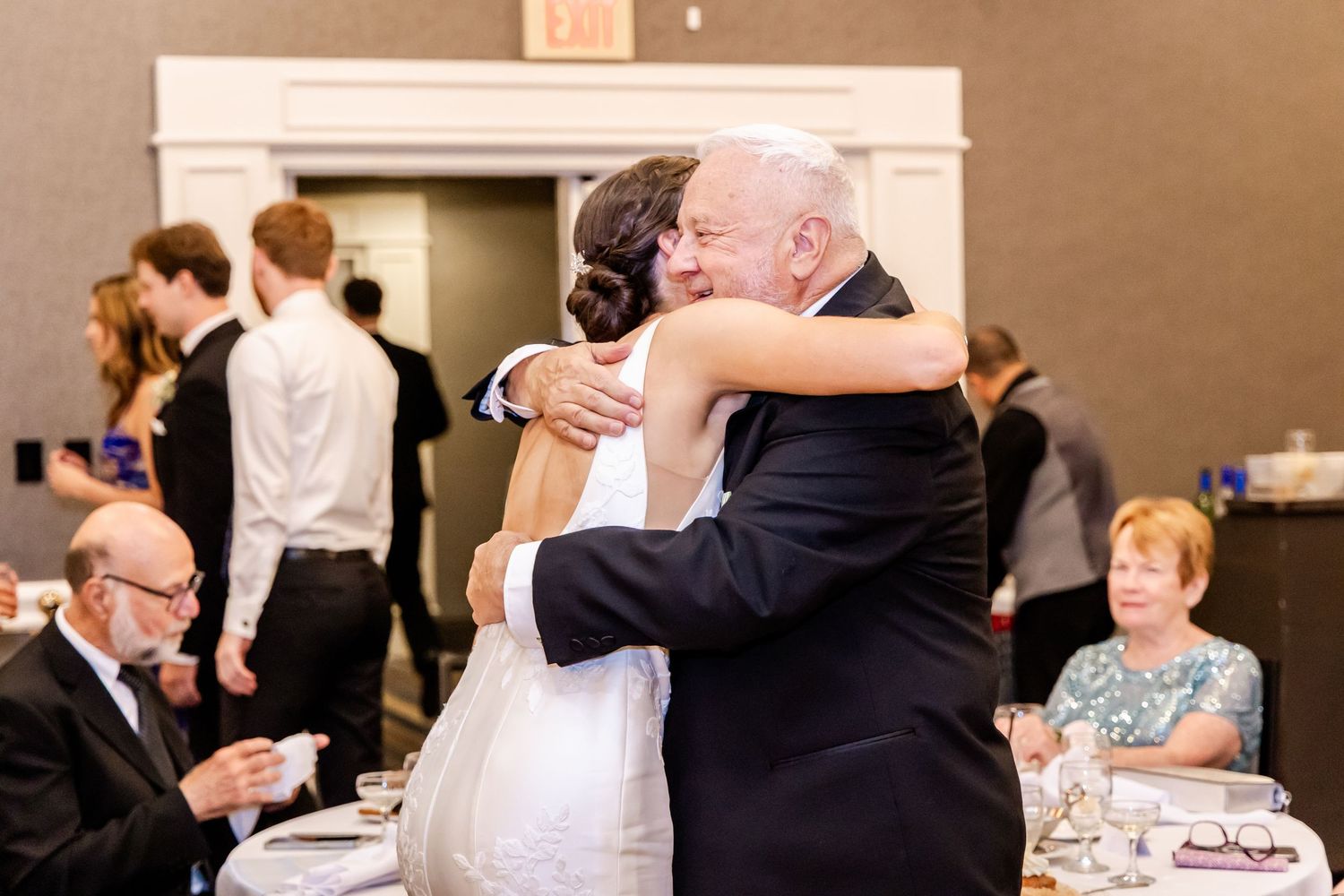 Wedding reception celebration with guests seated at decorated tables in an indoor venue.