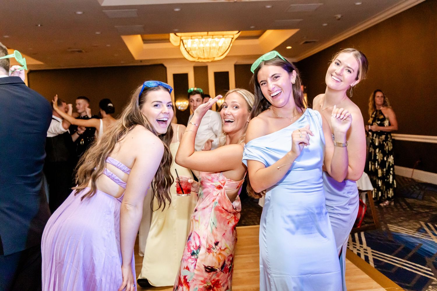 Wedding guests in pastel dresses pose playfully on the dance floor at an elegant reception.