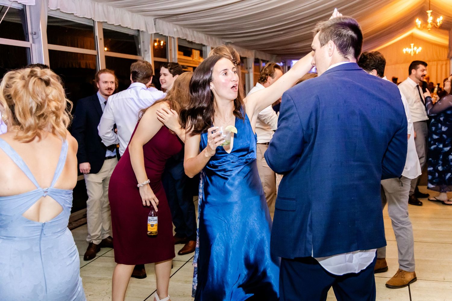 Wedding celebration with guests dancing under chandeliers and draped fabric ceiling.