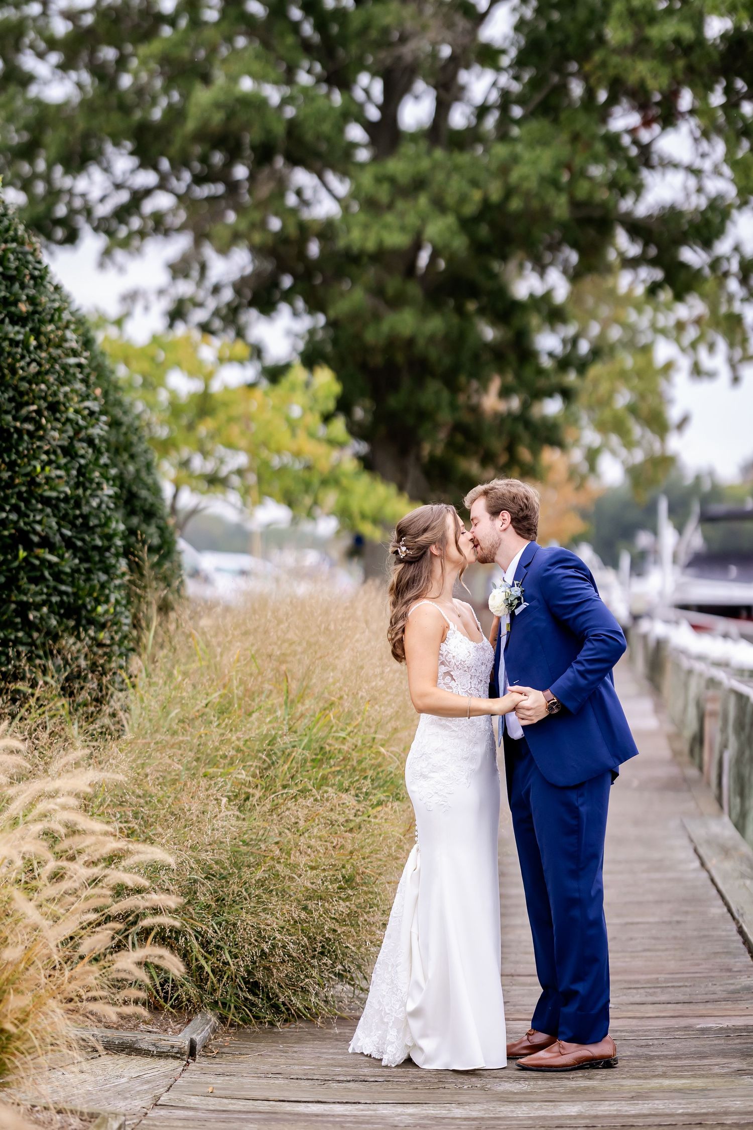 A romantic wedding couple shares intimate moments on a wooden boardwalk surrounded by tall grasses.