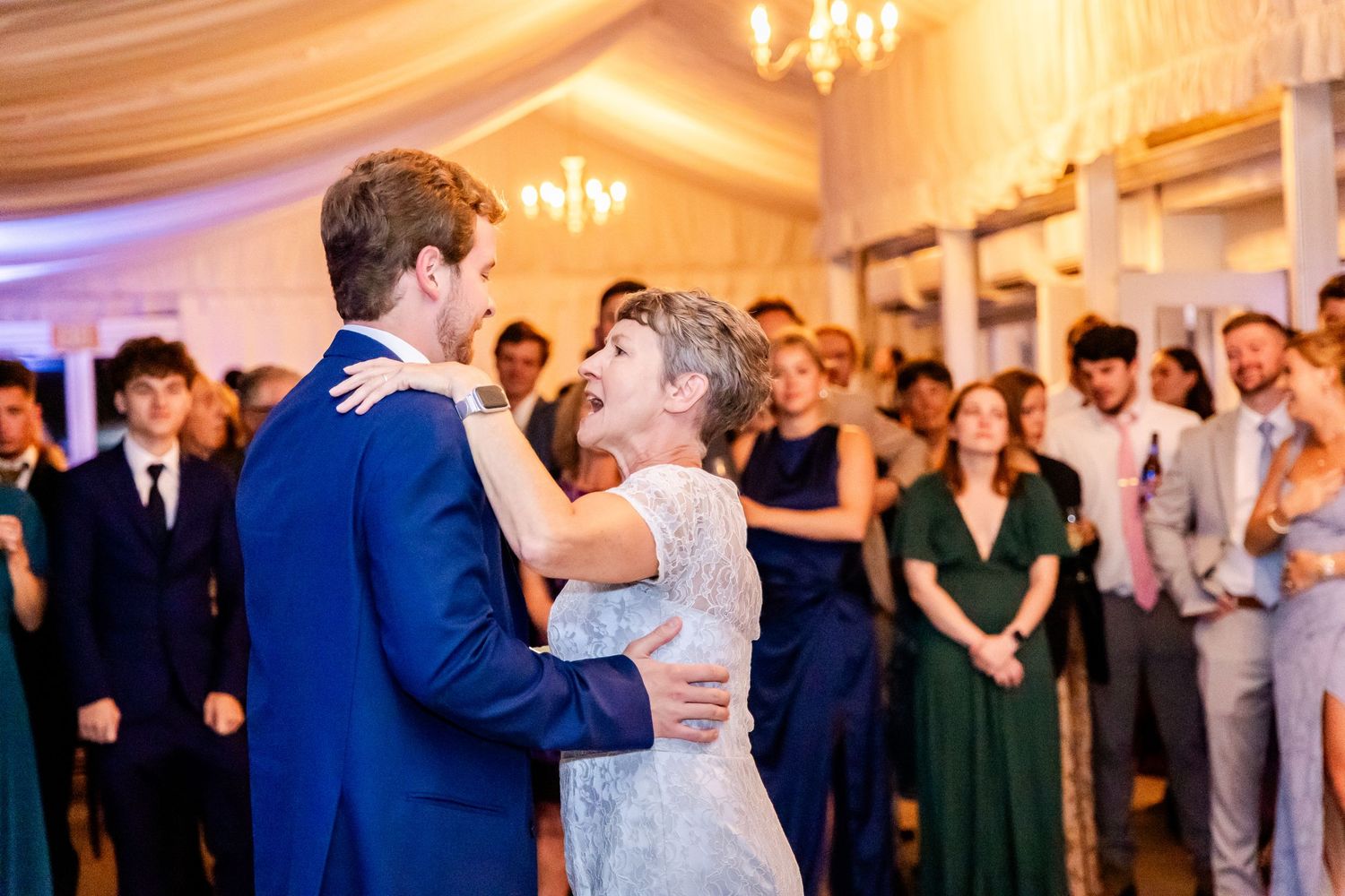 Wedding celebration in a ballroom with elegant chandeliers and draped ceiling decorations.
