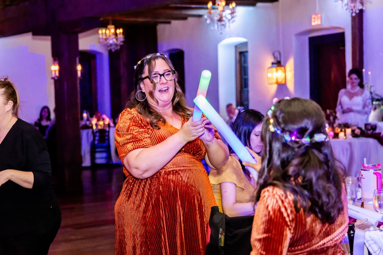 Wedding guests dancing and celebrating under purple and red mood lighting in an elegant reception hall.