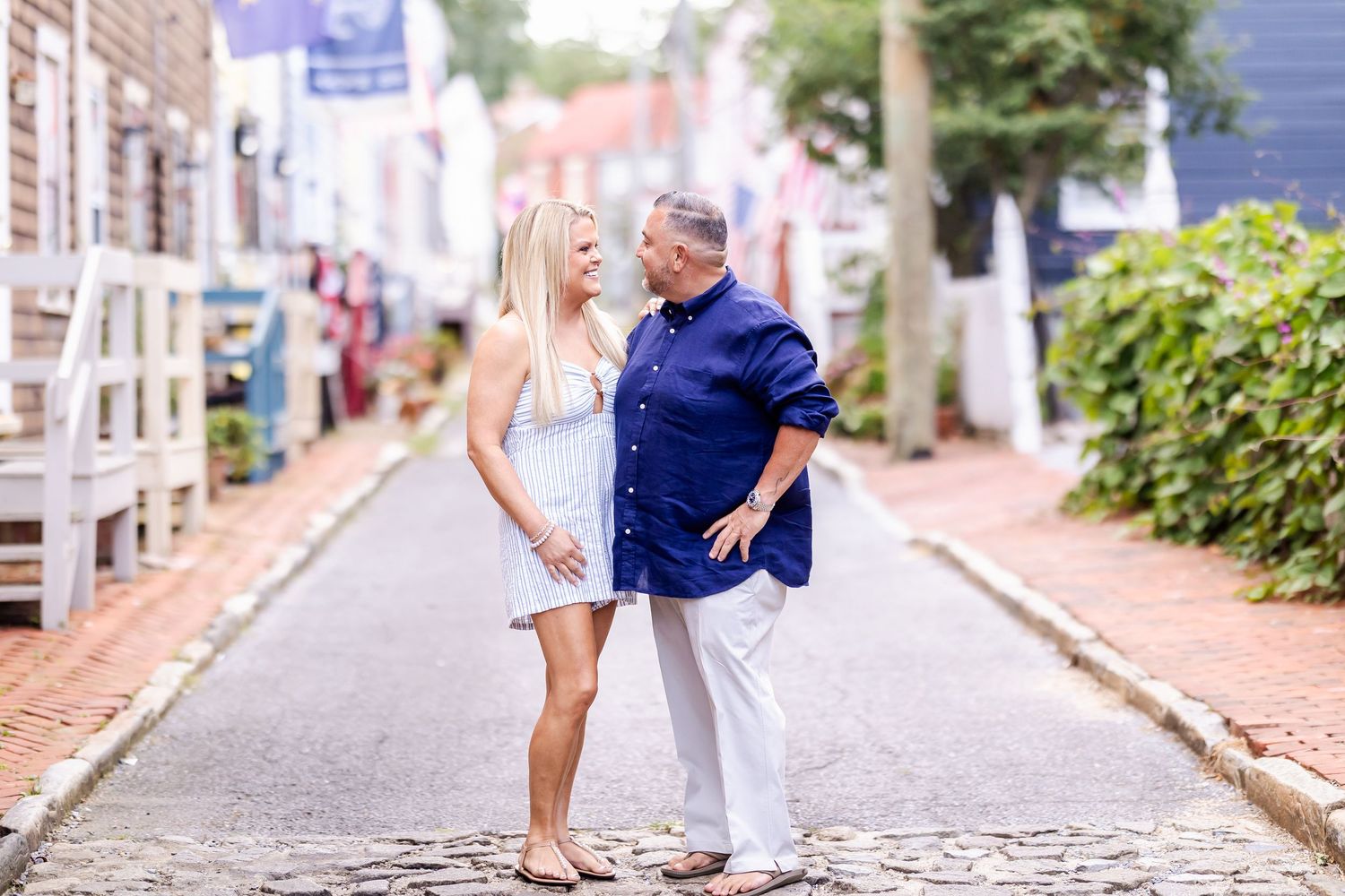 A couple shares a romantic moment on a charming cobblestone street lined with historic buildings and greenery.