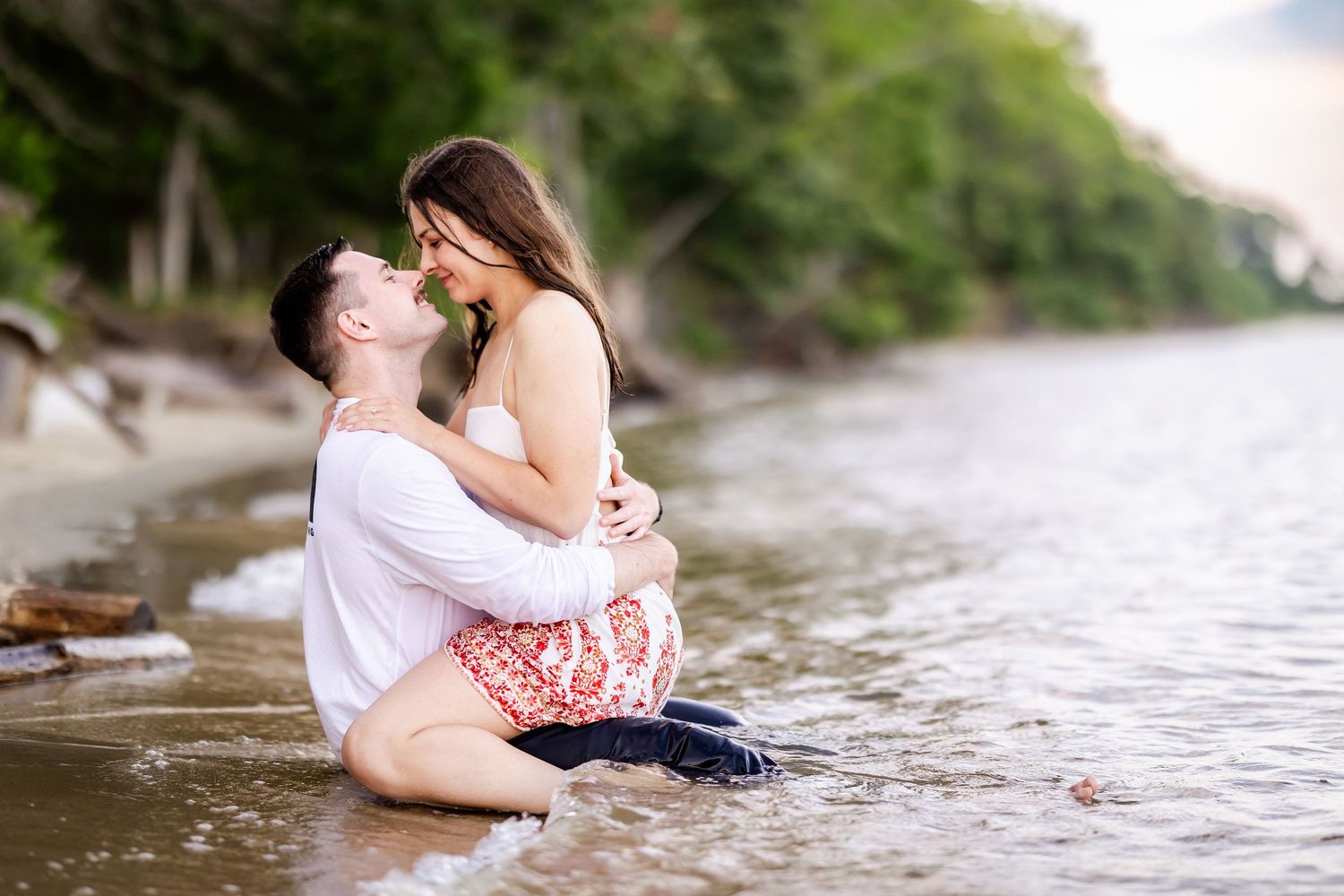 Romantic couple embraces while sitting at the edge of a tranquil lake shore on a sunny afternoon.