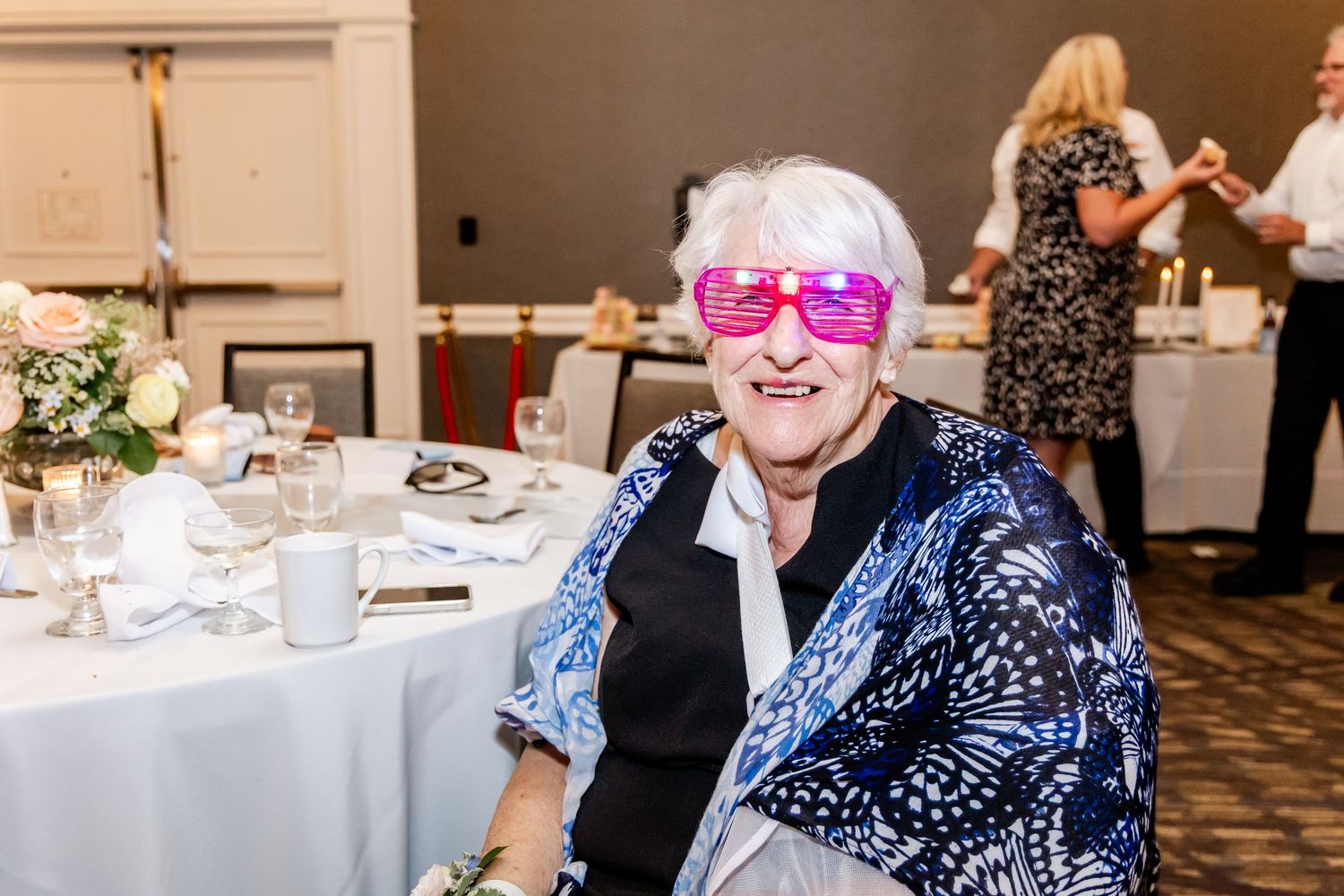 Guest wearing bright pink glasses enjoys wedding reception at decorated table.