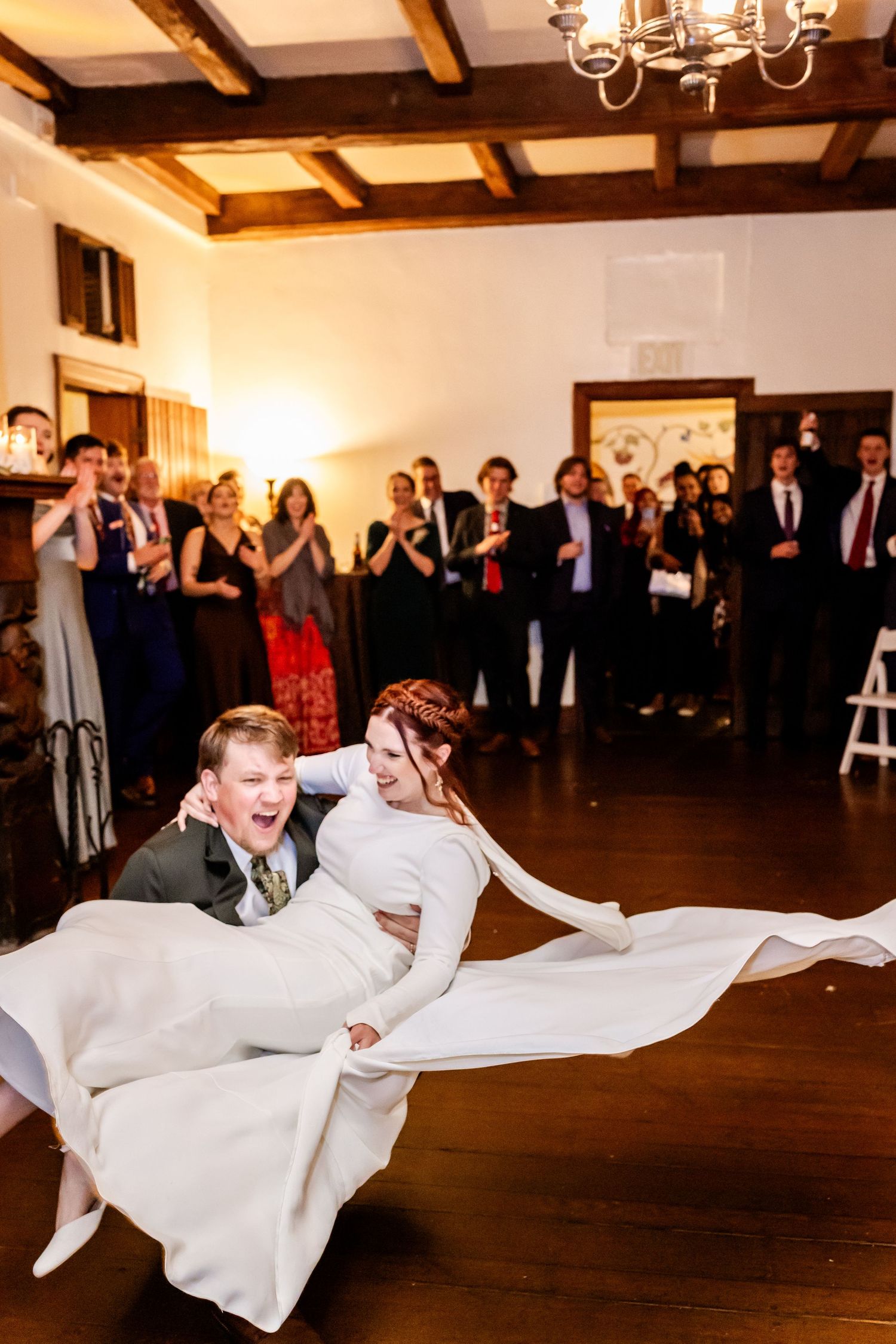A couple performs an elegant dip during their first dance at a wedding reception while guests watch from the background.