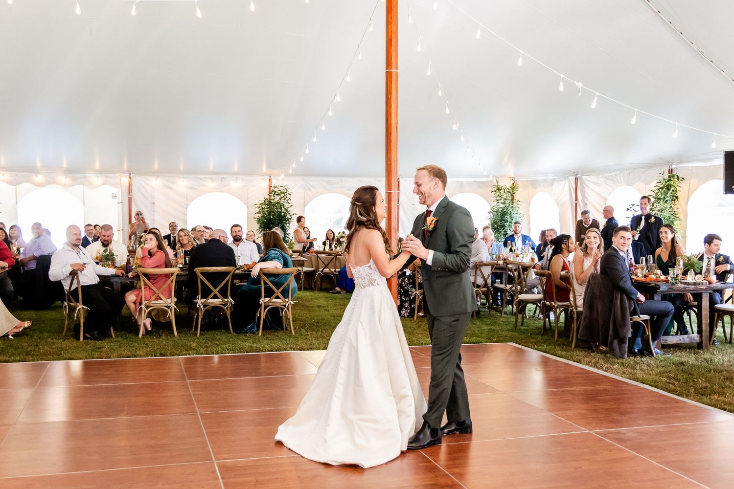 Wedding reception under white tent with string lights and dining tables.