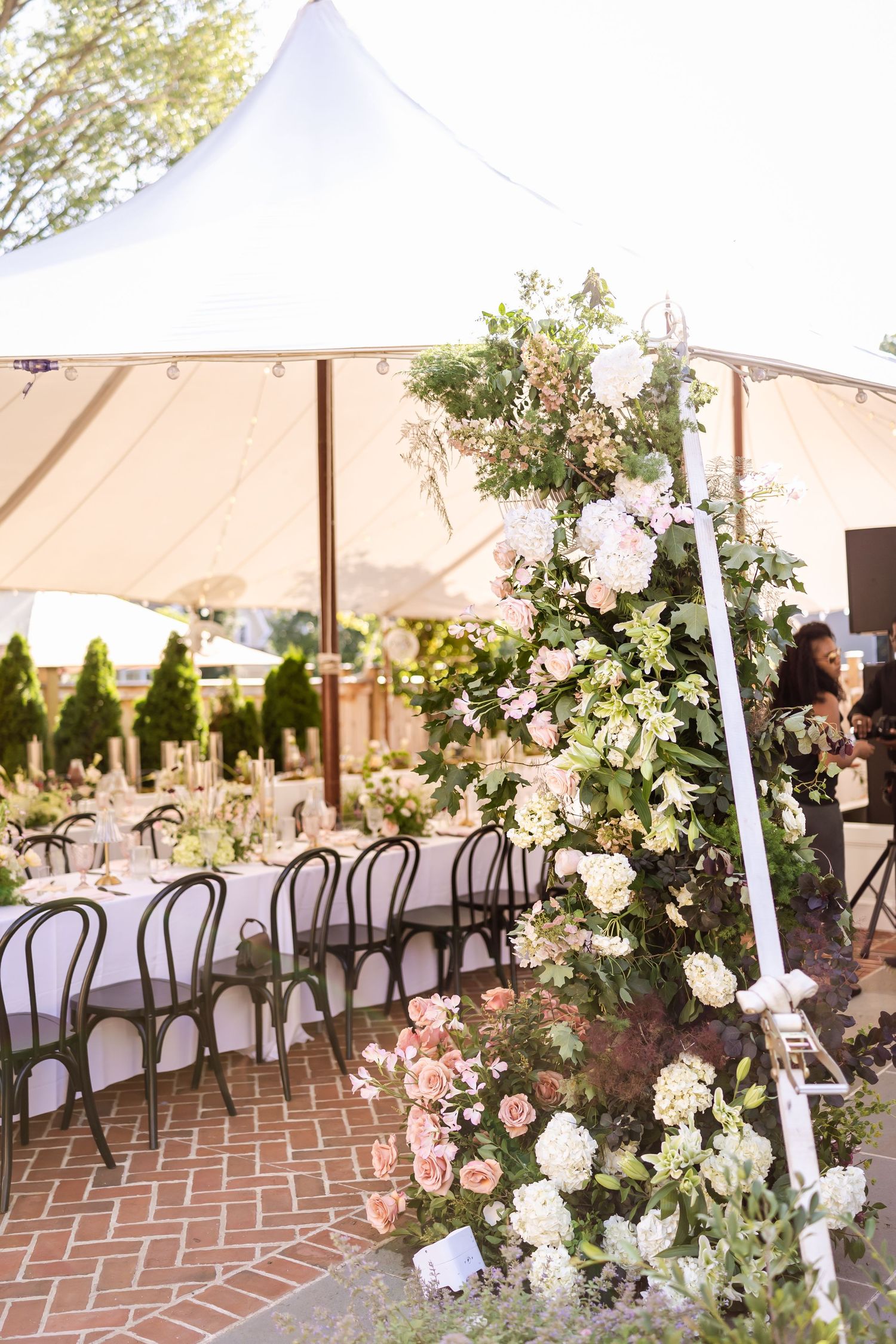 Elegant outdoor reception setup with long tables under a white tent adorned with floral arrangements.
