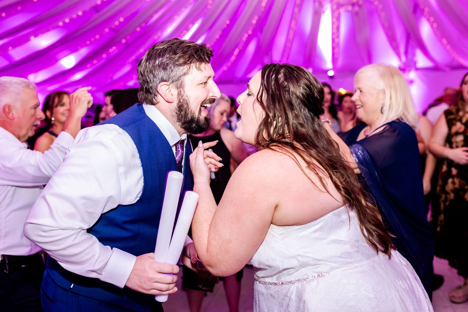 A couple singing passionately together on the dance floor under vibrant pink lighting at their wedding reception.