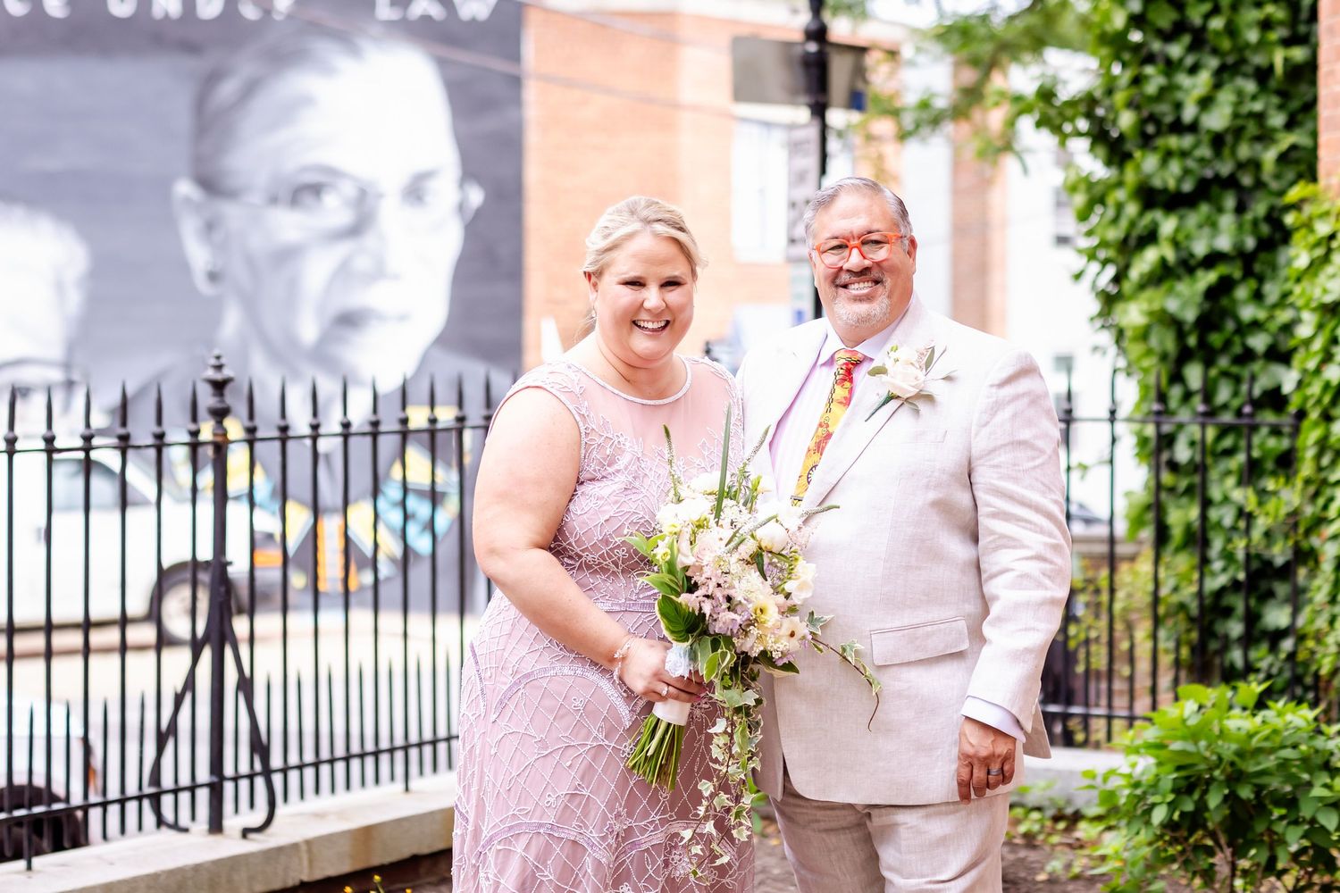 Elegant wedding portrait against brick wall with iron fence and garden background.