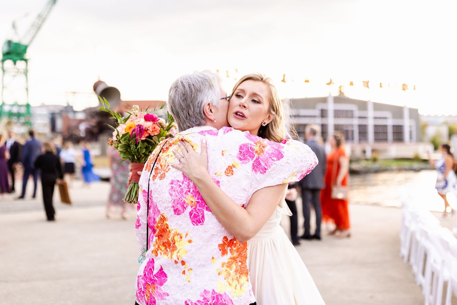 Emotional embrace during outdoor wedding celebration with industrial backdrop.