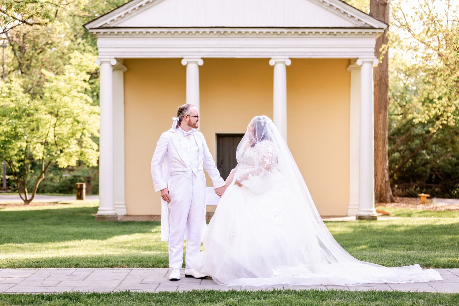 Wedding couple poses in front of yellow neoclassical building with white columns and portico on their special day.