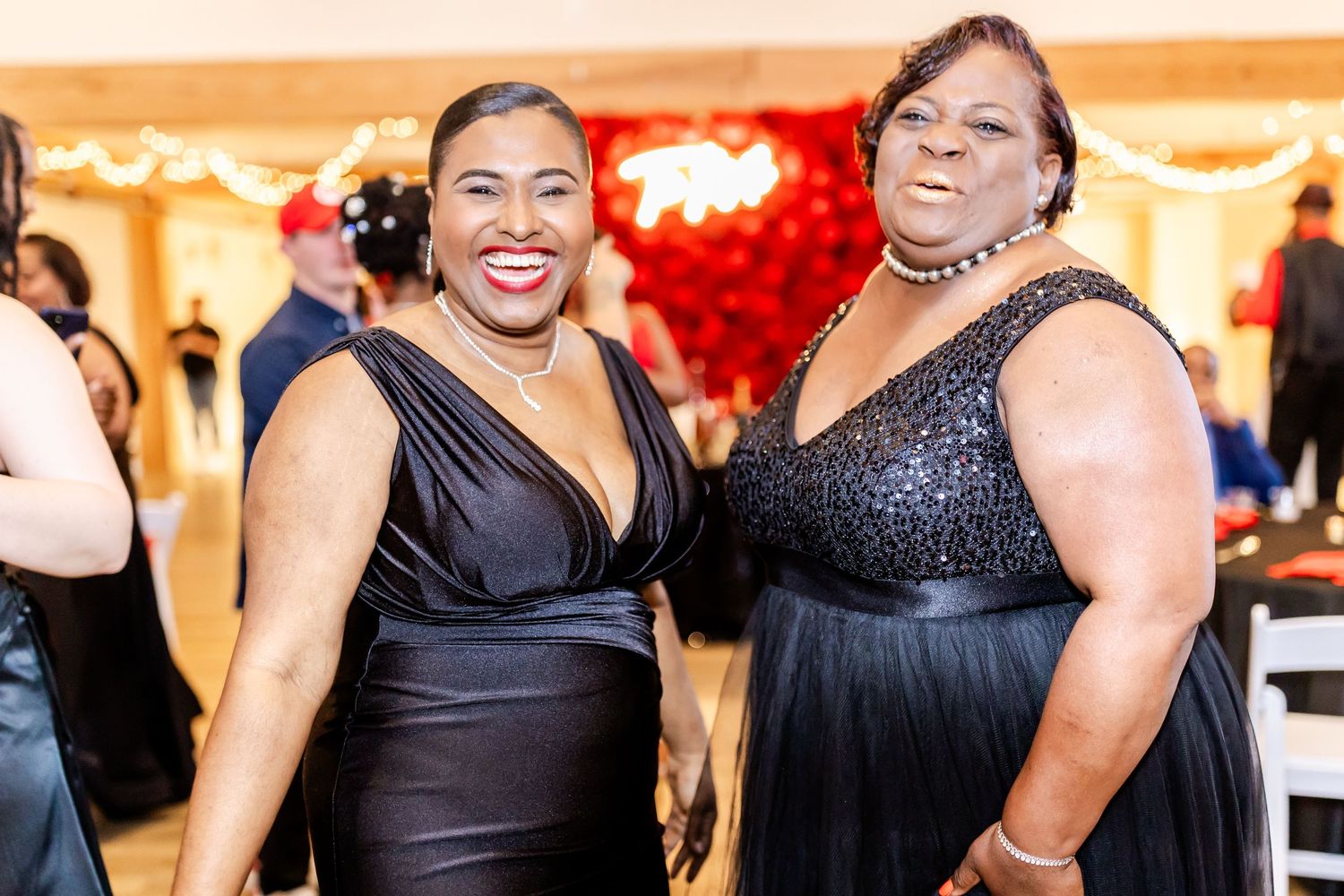 Wedding guests in elegant black formal wear smile during reception celebration.