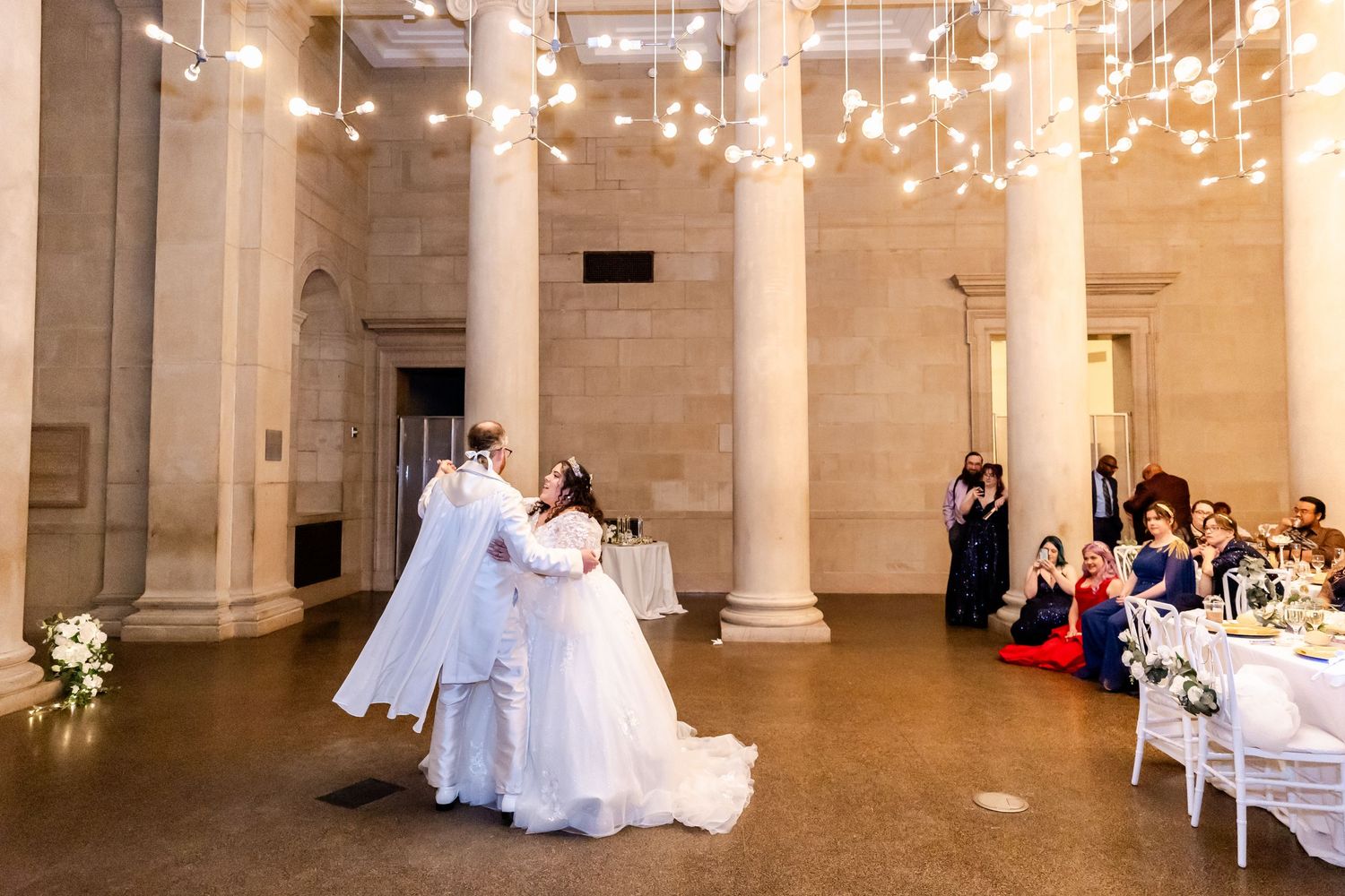 A couple shares their wedding dance in a historic venue with beautiful hanging lights.