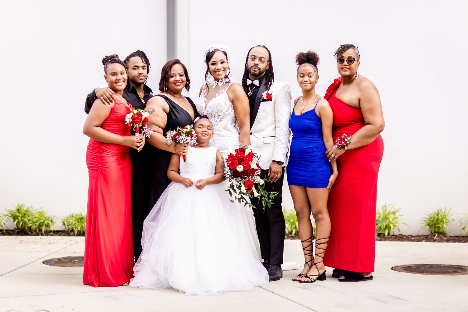 Large wedding party in coordinated red, white, and black attire pose together outdoors.