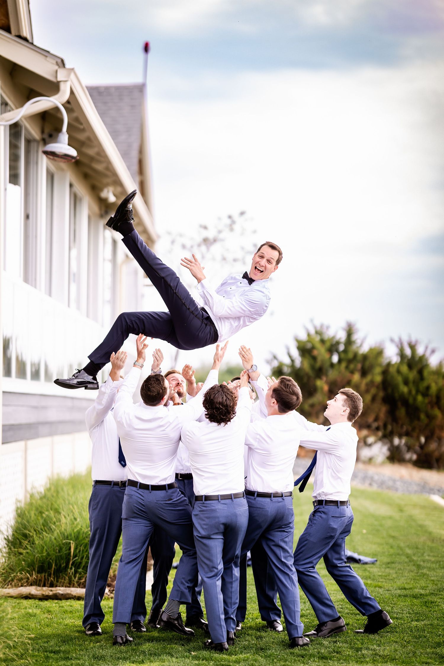 Groomsmen toss groom in air during fun outdoor wedding photo session.