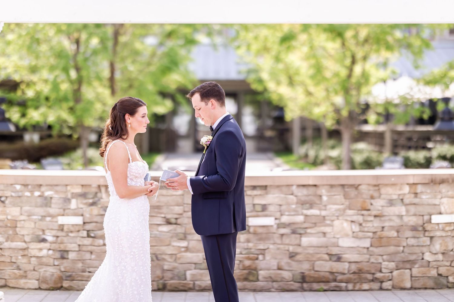 A couple in wedding attire shares a romantic moment in front of a stone wall during their outdoor celebration.