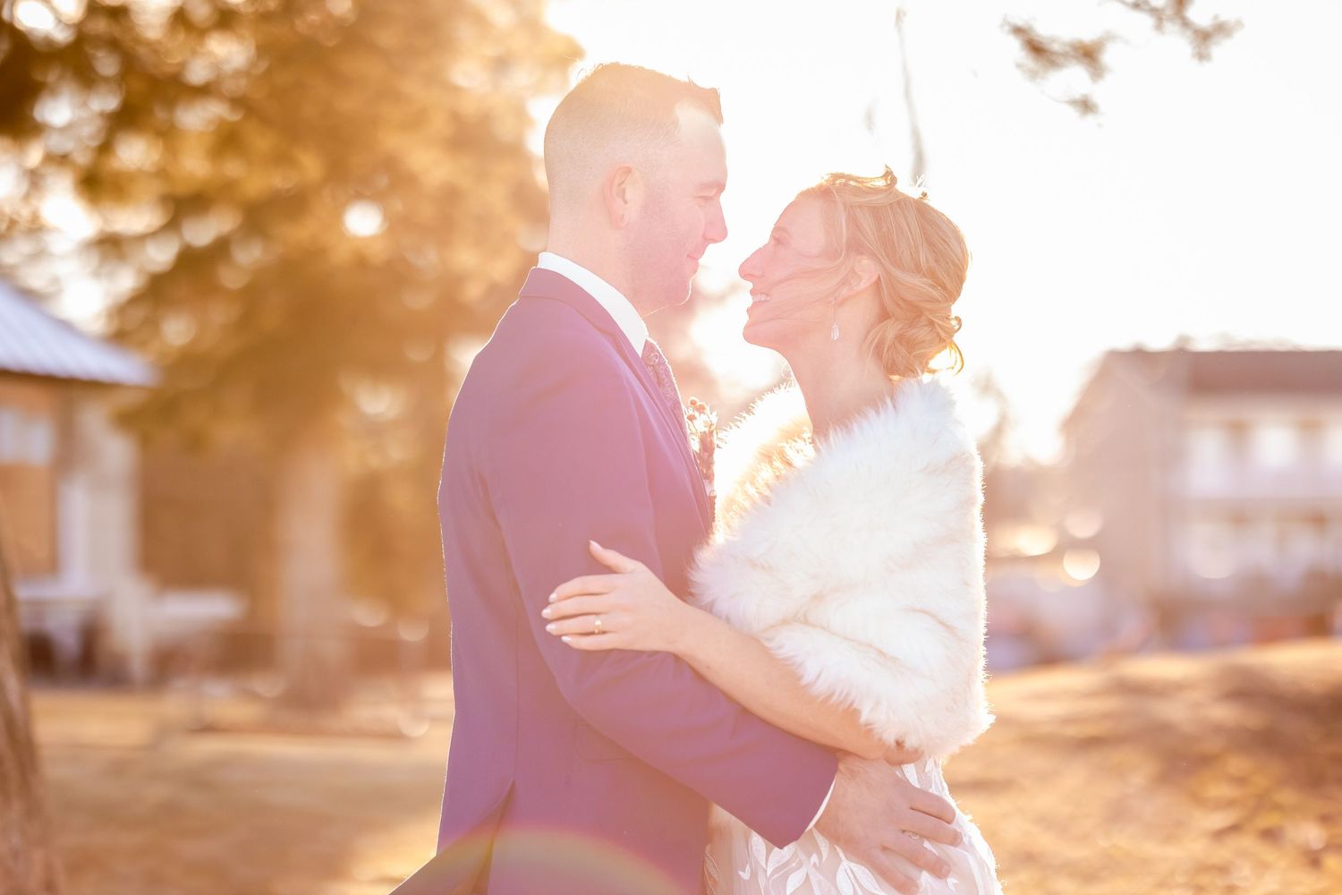 Two people embrace during golden sunset hour outdoors with soft sunlight glowing behind them.