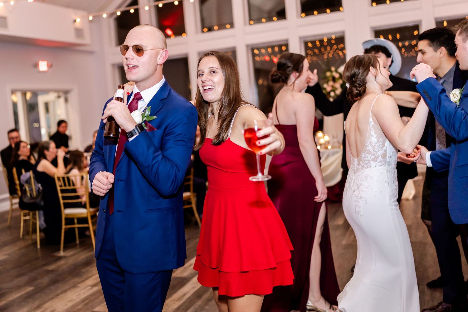 Wedding reception scene with guests in formal attire dancing and holding drinks.