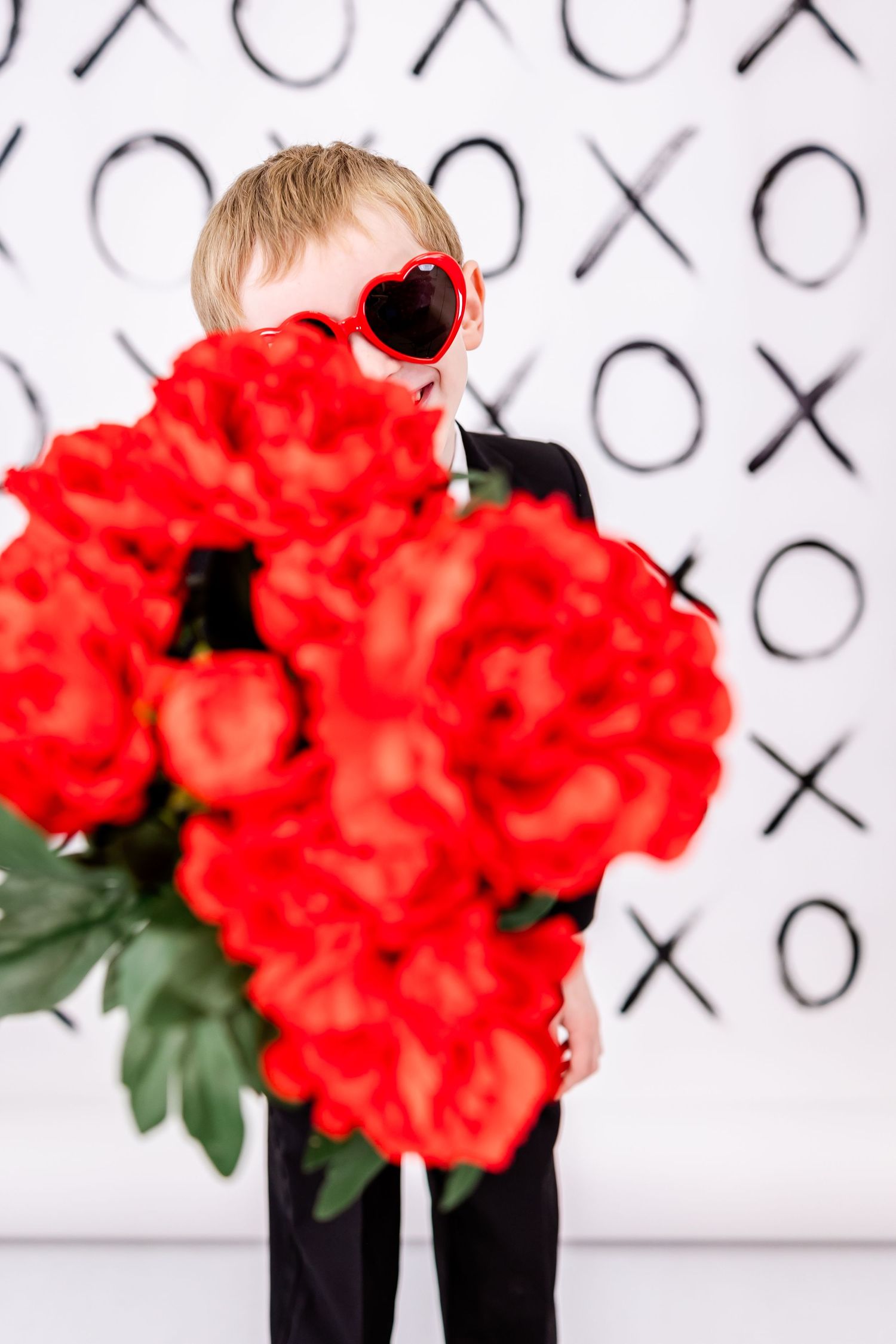 Red heart sunglasses and vibrant red roses stand out against black and white XO patterned background.