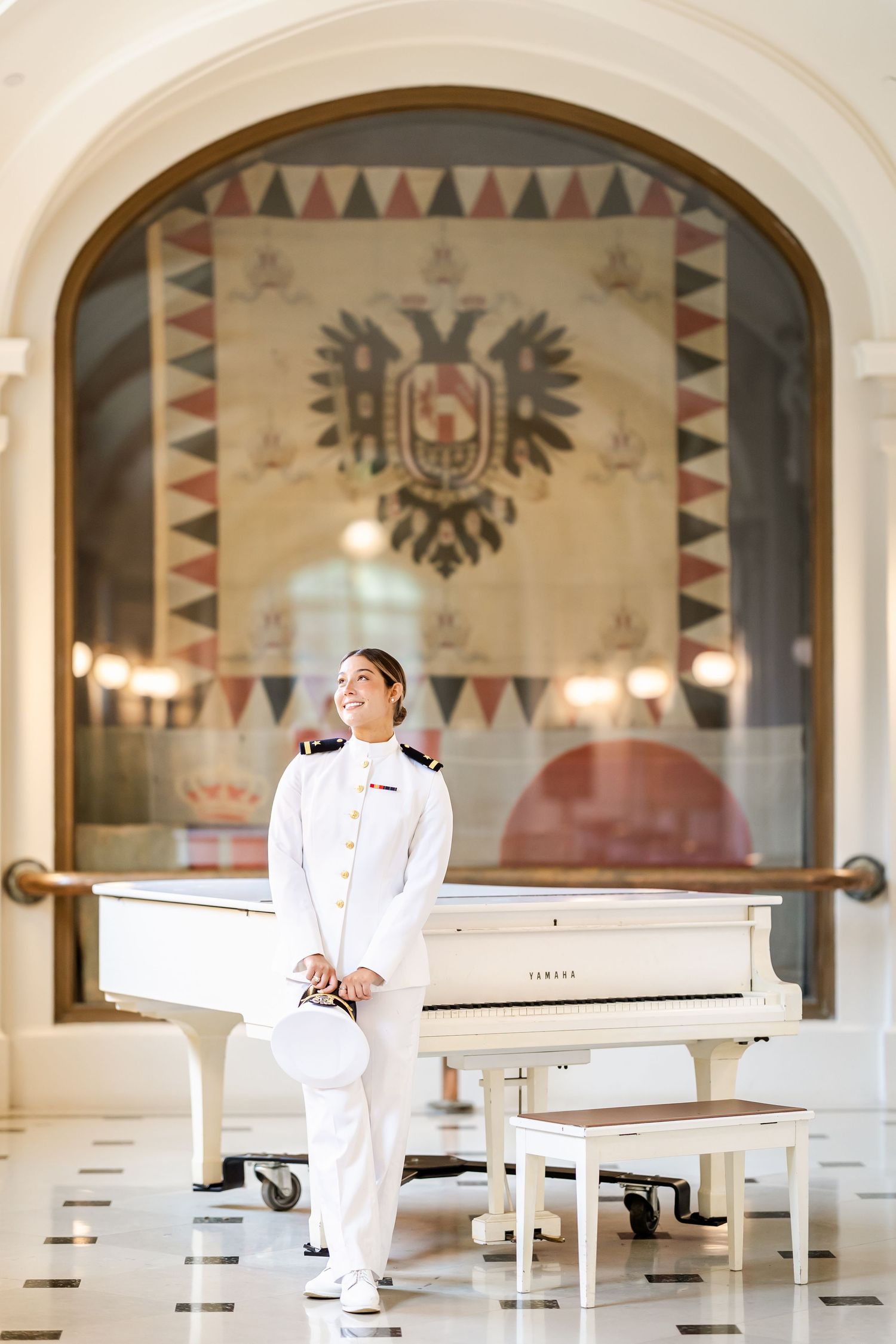 Military service member in white dress uniform seated in elegant room with decorative arched windows and wall designs.