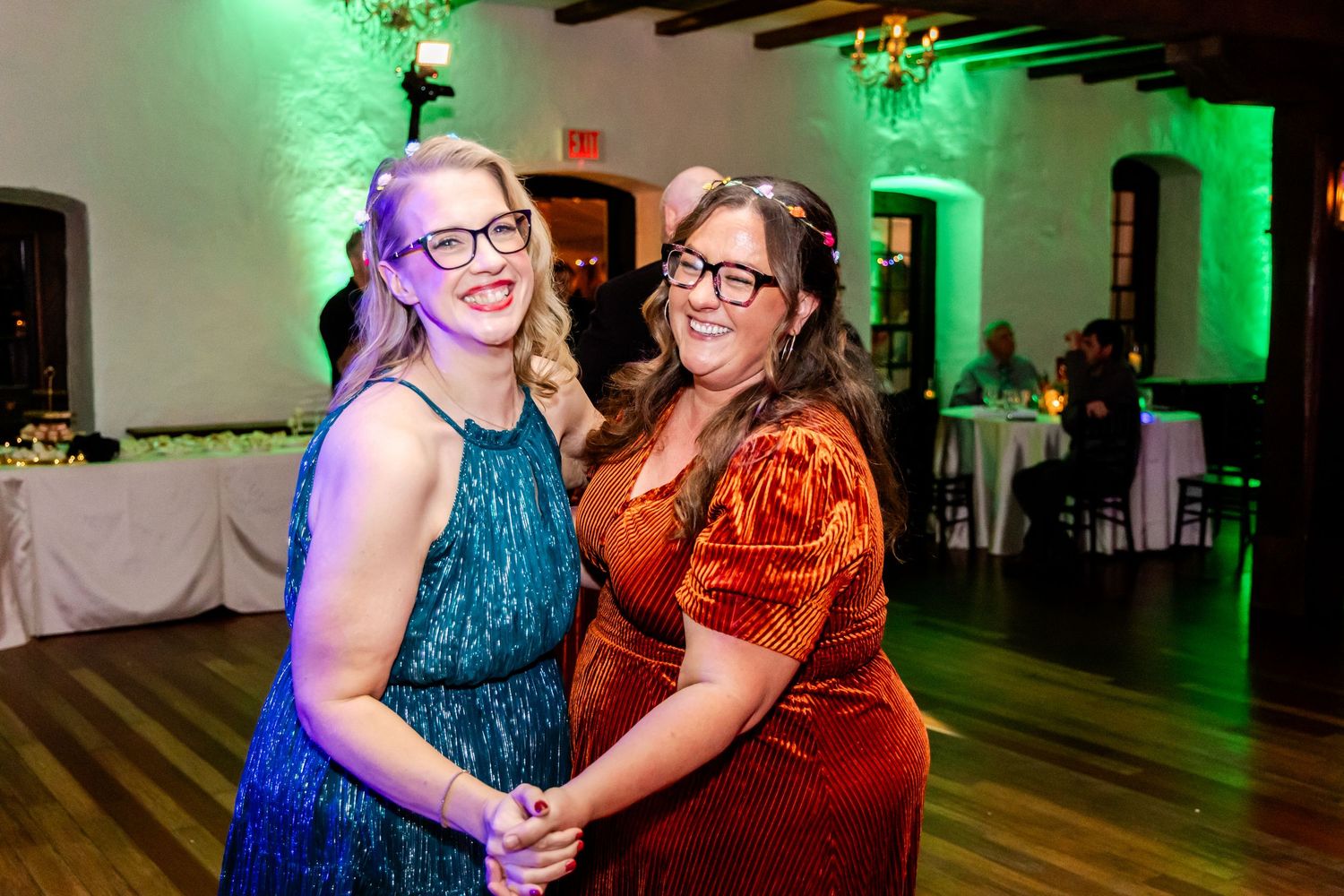 Two people dance together on a hardwood floor with green uplighting and elegant decor at an indoor venue.