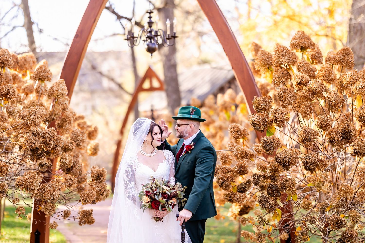 A wedding couple embraces under a wooden arch surrounded by golden autumn foliage.