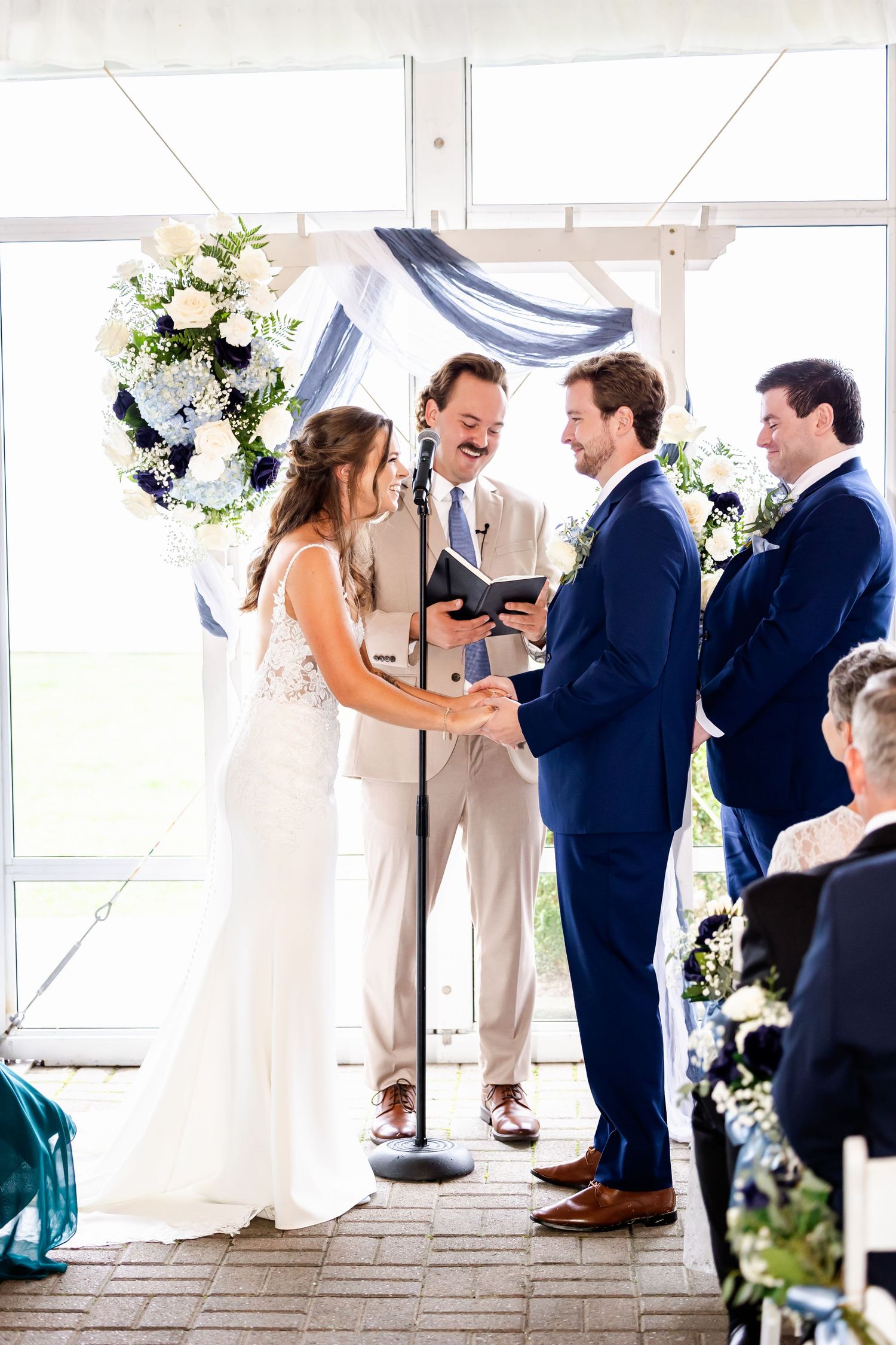 Wedding ceremony in a bright white tent with elegant floral decorations and gathered guests.