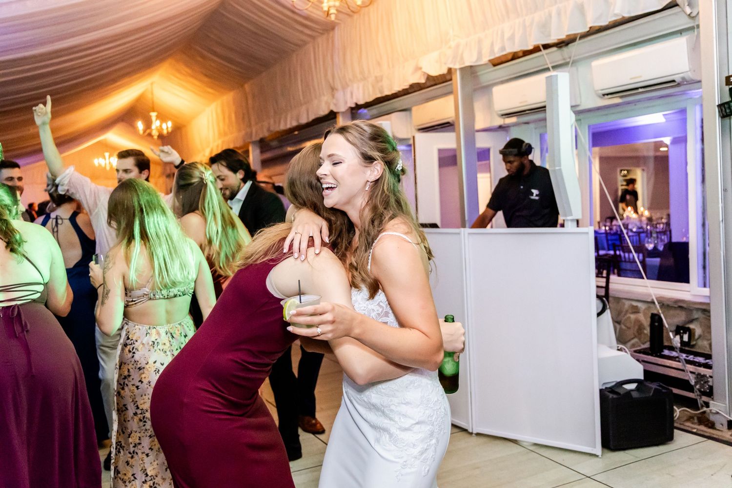Wedding party dancing and celebrating at evening reception under draped ceiling with purple lighting.