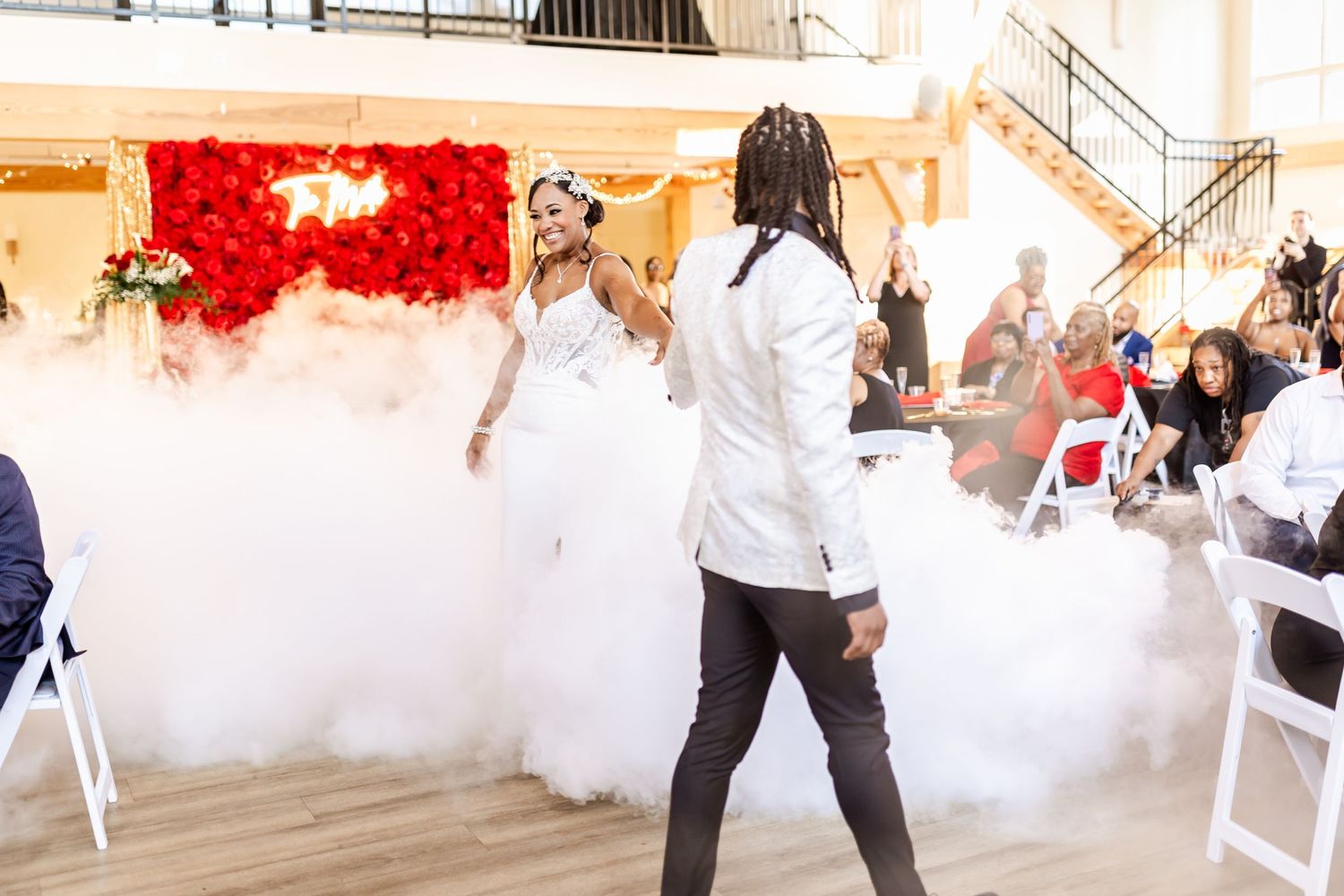 Wedding couple performs energetic dance move amid fog effects at indoor reception.