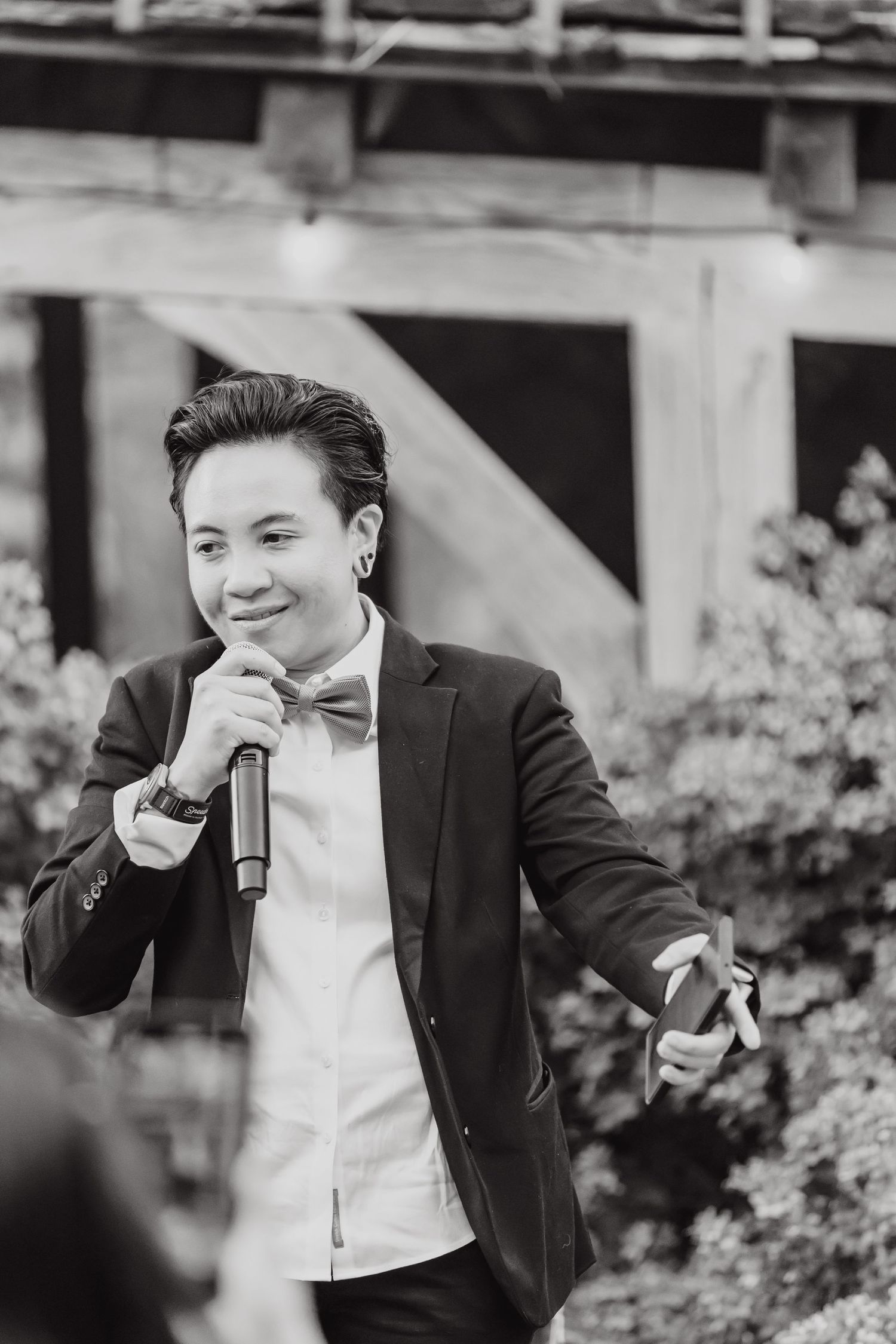 Wedding speaker holding microphone and gesturing during outdoor reception speech.