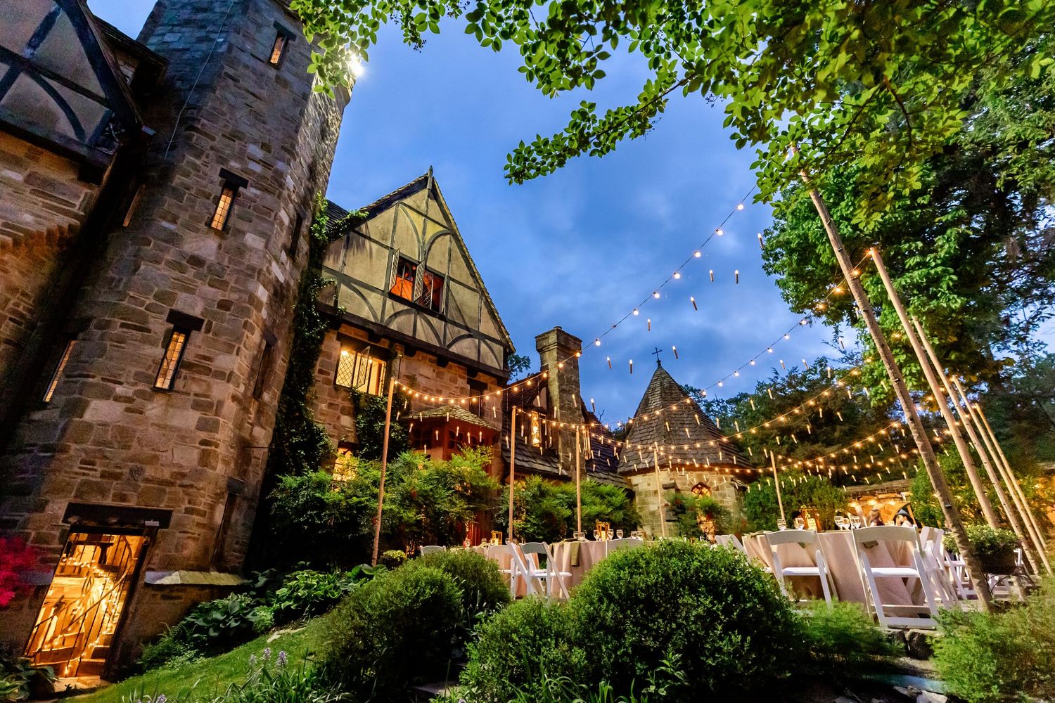 Castle-like venue with manicured gardens set up for outdoor dining under string lights.