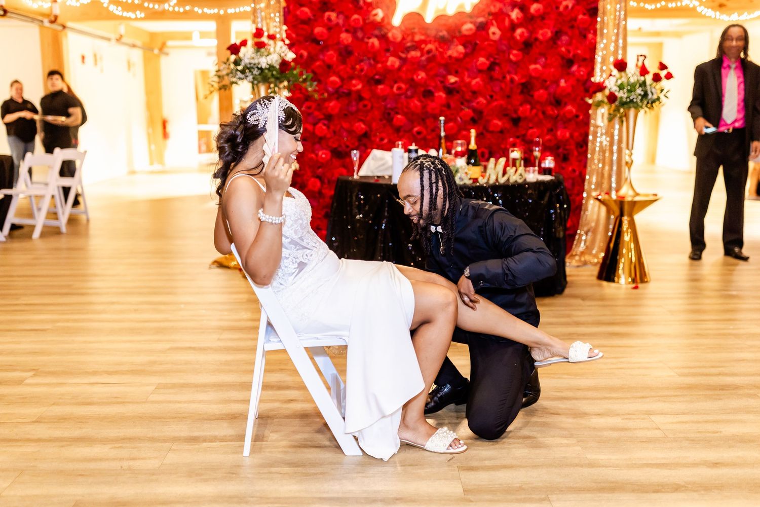 Wedding reception scene with a dramatic red balloon wall and white chairs on hardwood floors.