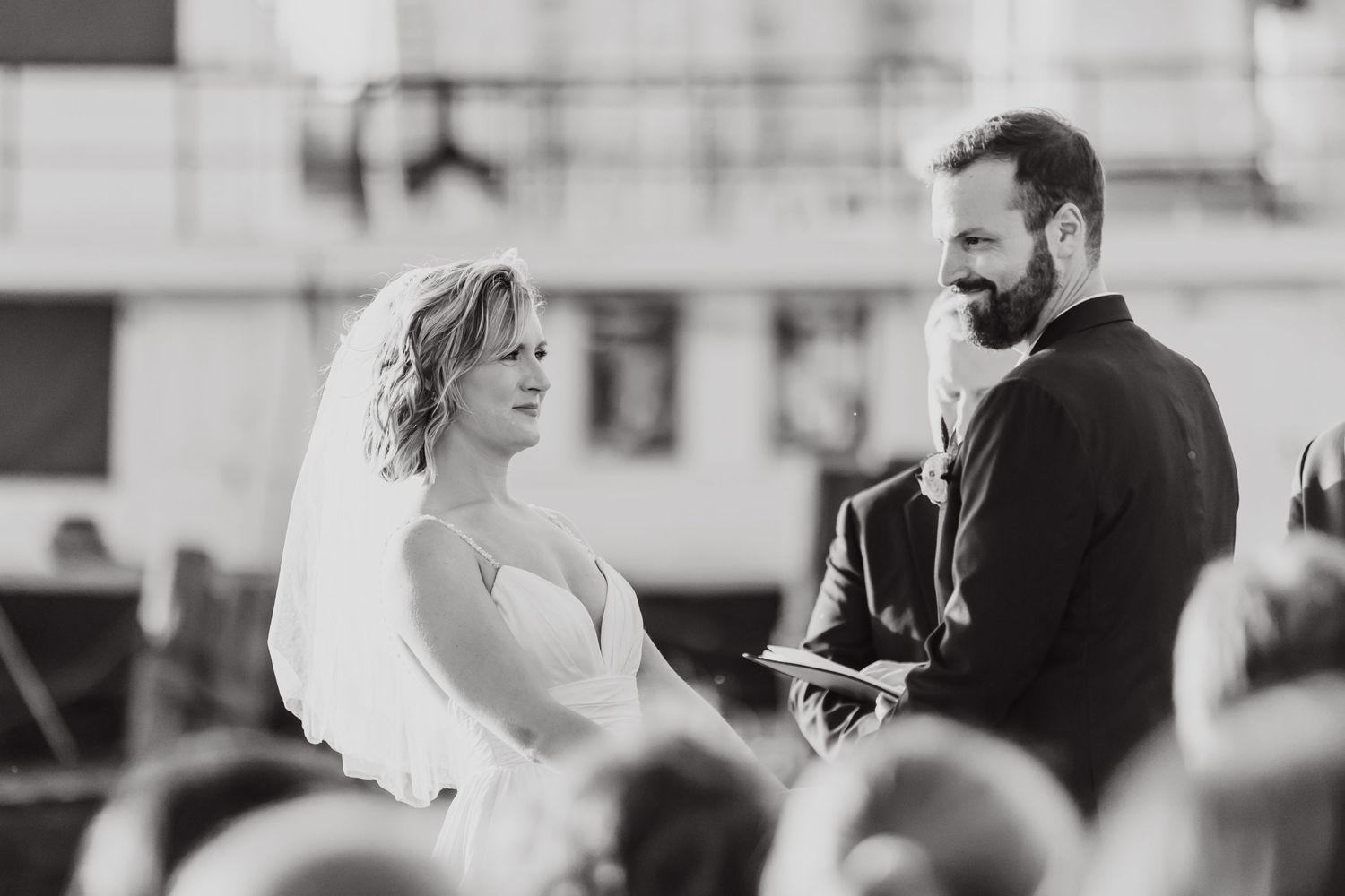 Black and white ceremony photo with gathered guests in background during outdoor wedding.