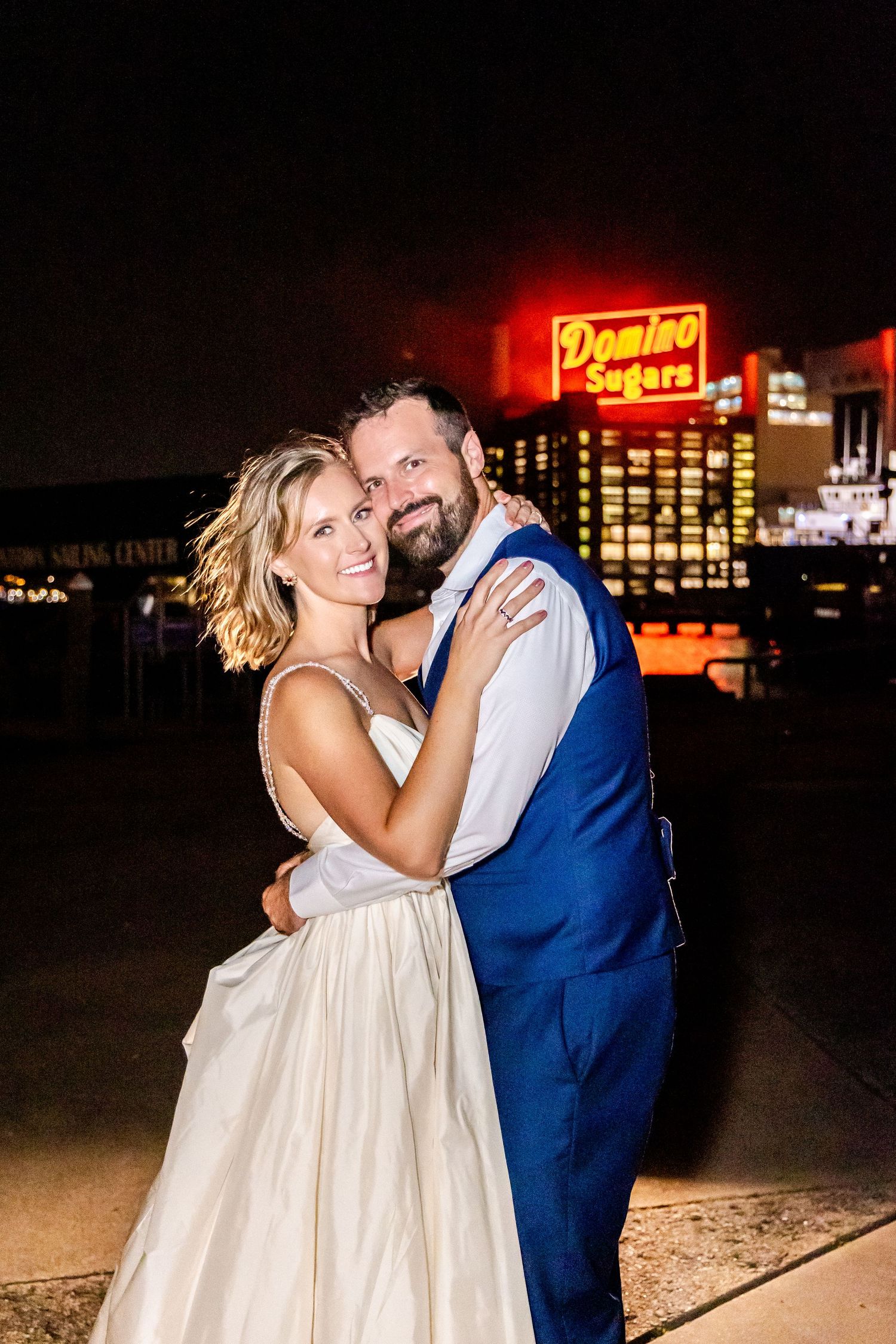 Evening portrait of couple embracing under glowing neon hotel signage.