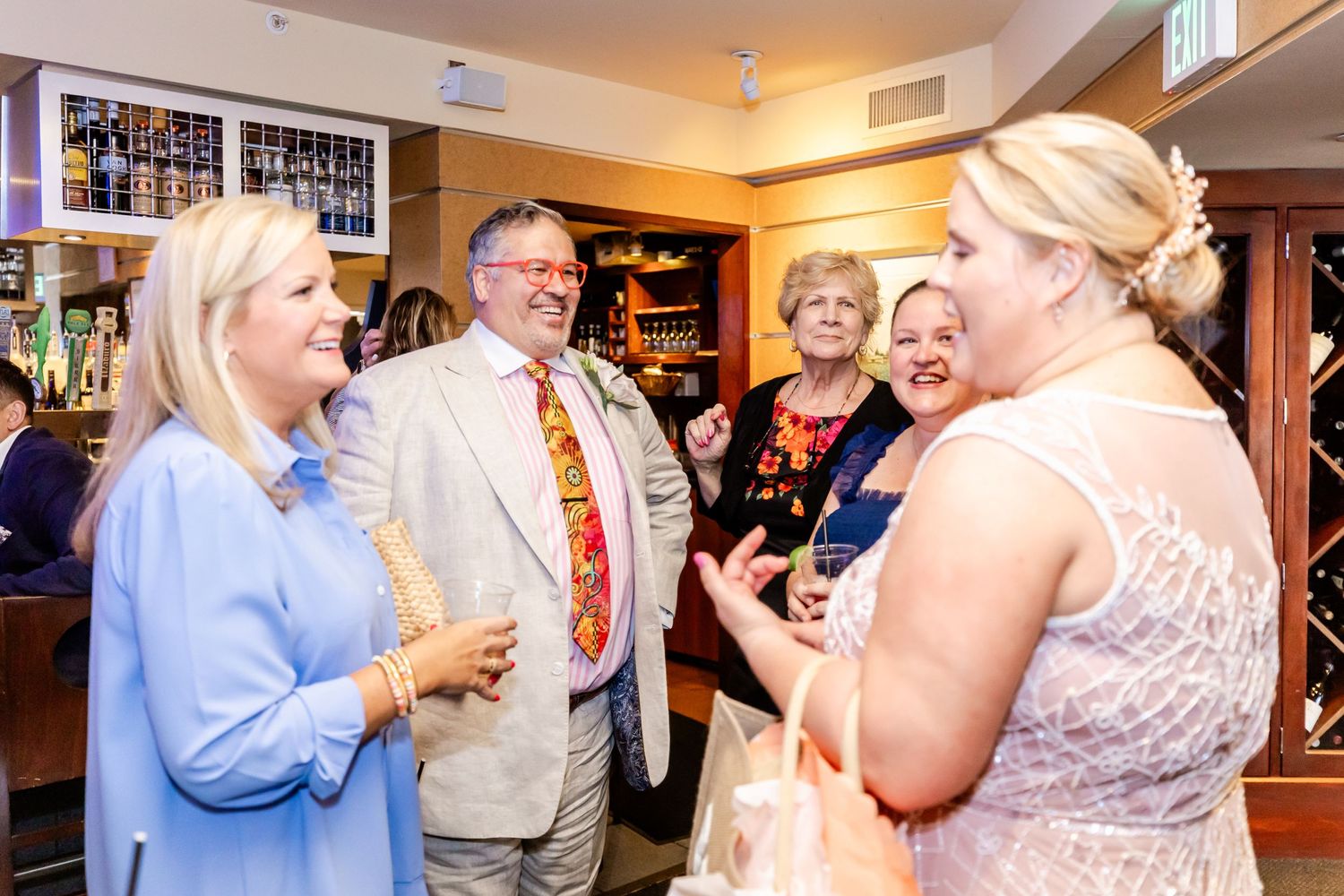 Social gathering with guests enjoying lively conversation near a bar with bottles displayed.