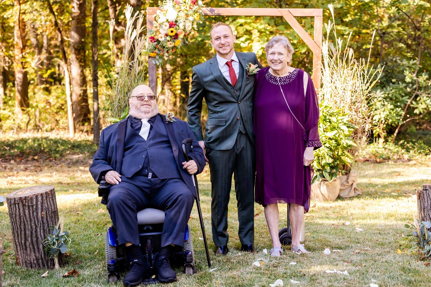 Wedding party gathered outdoors with purple bridesmaid dresses under autumn trees.
