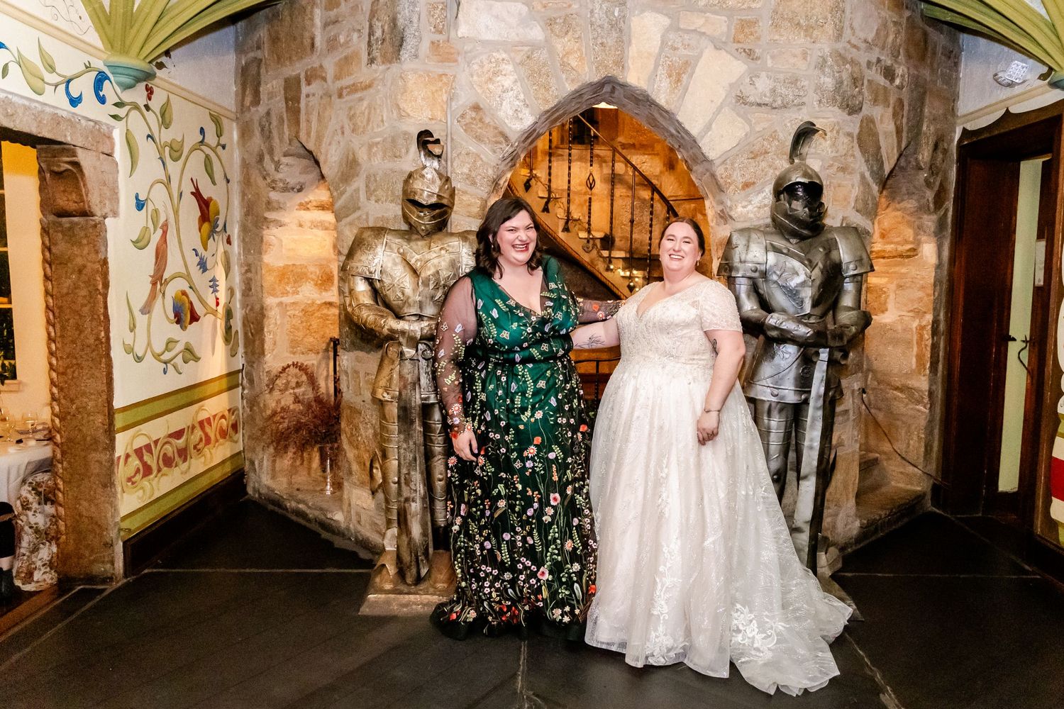 Celebrating guests pose with decorative knight statues in an ornate stone hallway.
