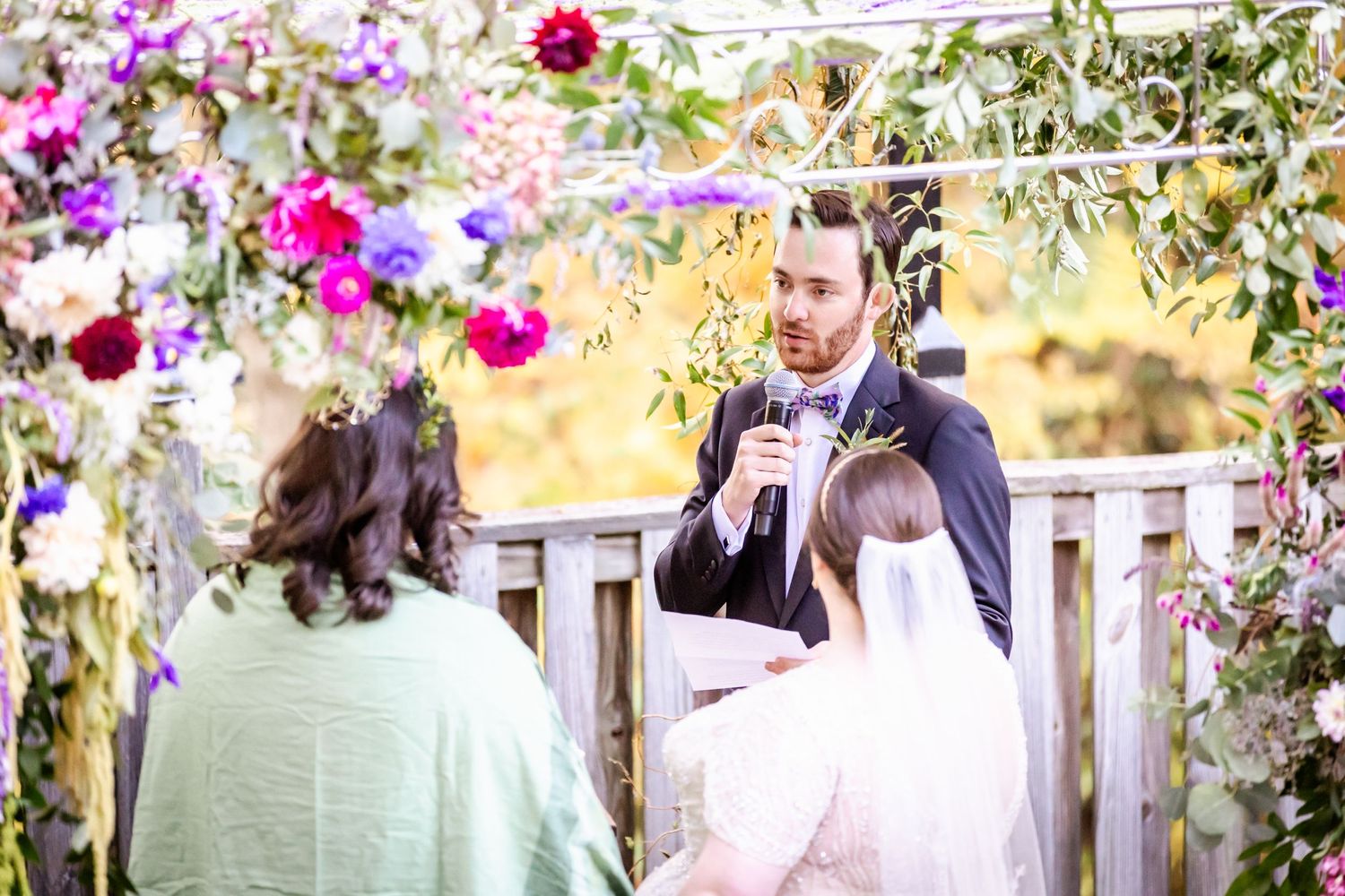 Outdoor wedding ceremony under floral arch with vibrant pink and purple blooms.
