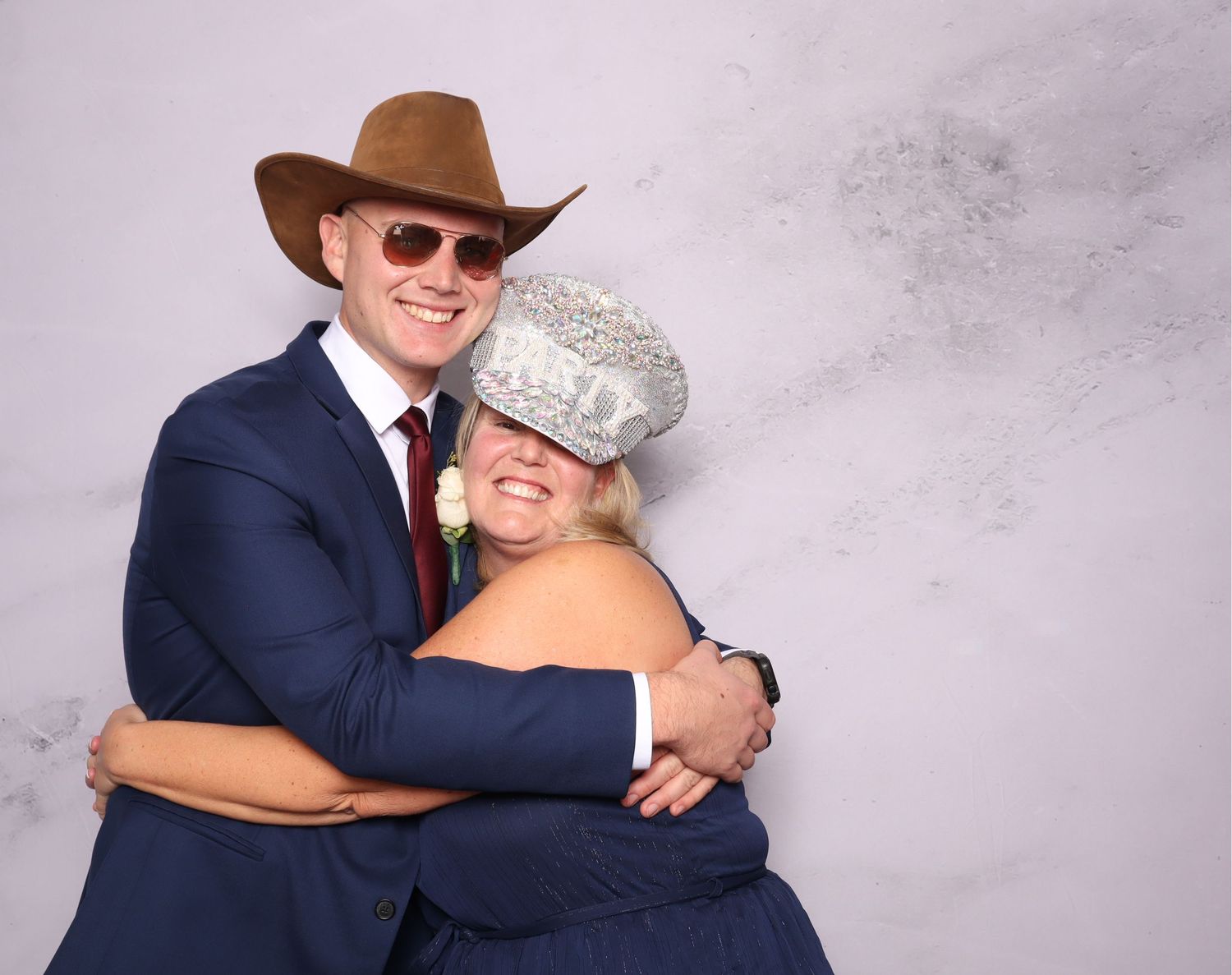 Couple in formal wear with cowboy hat and sparkly accessories posing at a photo booth.