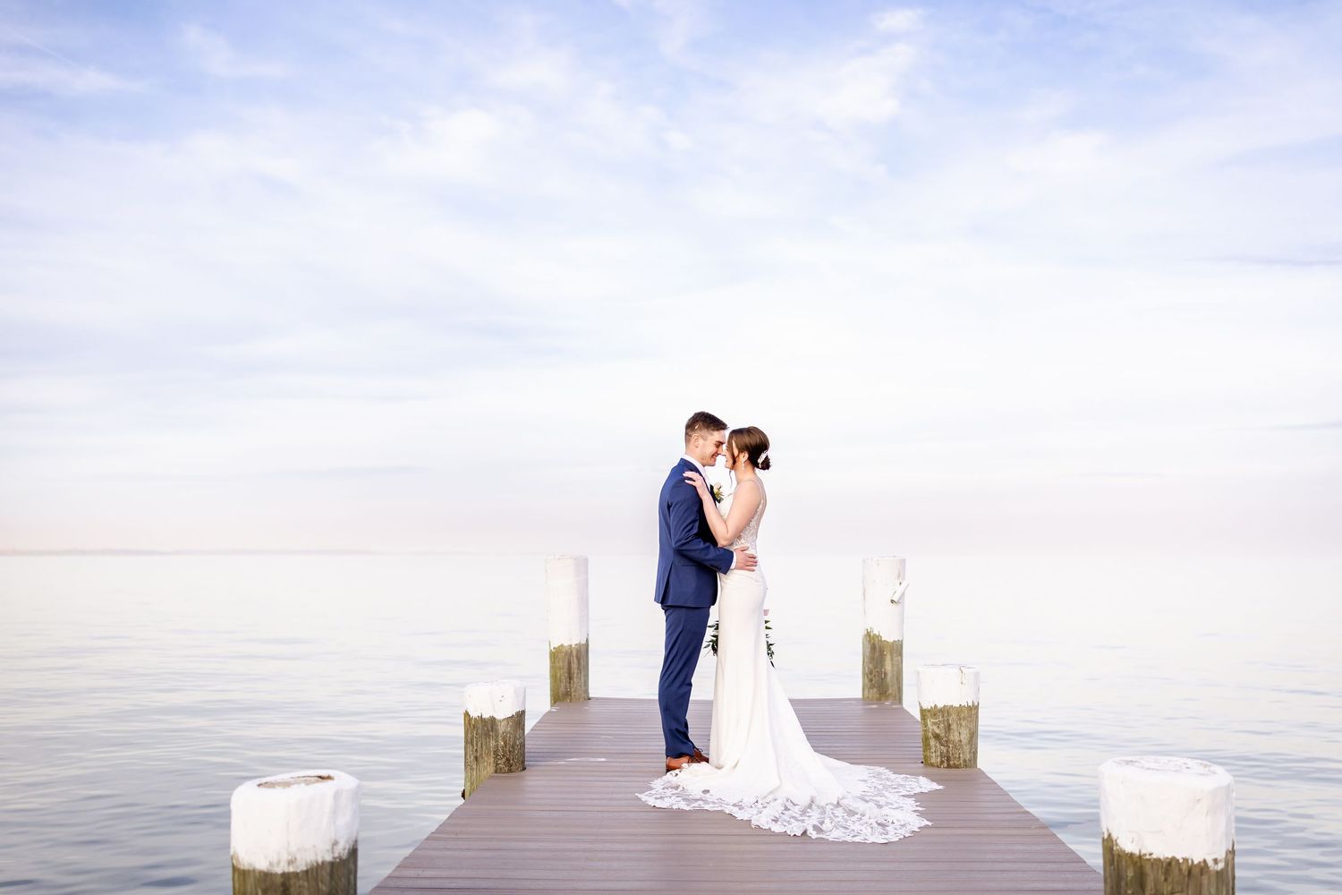 Wedding couple shares romantic moments on a wooden pier overlooking calm waters at sunset.