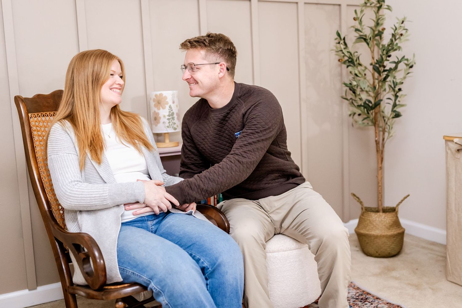 A couple shares a joyful moment while sitting together in a wooden rocking chair next to a potted plant.