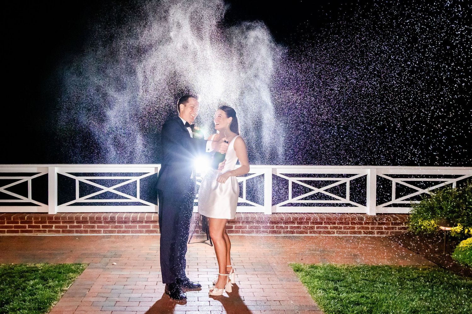 Couple poses under white trellis archways at dusk for dramatic wedding photos.
