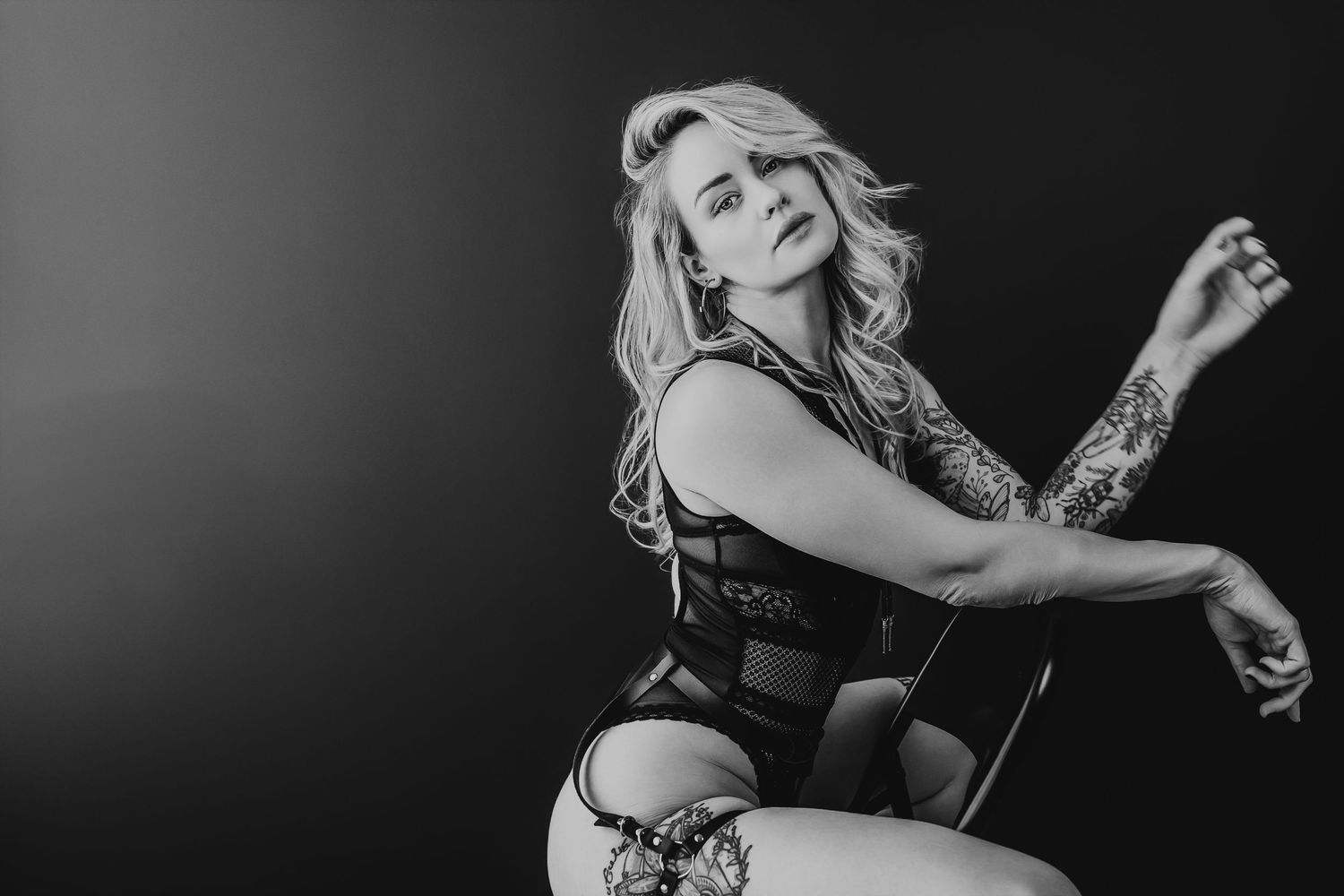 Black and white boudoir style artistic portrait featuring a woman in lingerie posing gracefully in dramatic lighting.