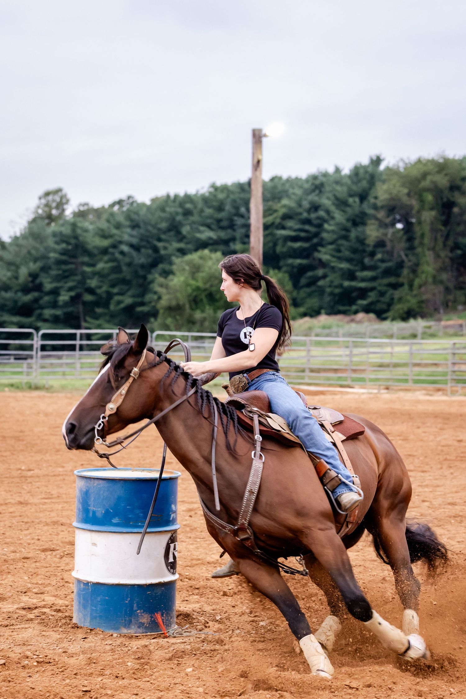 Horse and rider executing sharp turn around barrel during daytime practice in sandy arena.