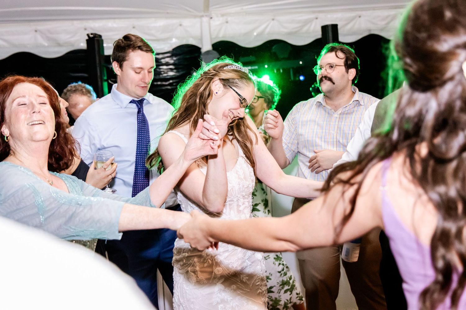 Wedding party guests dance and celebrate on a crowded dance floor under colorful lighting.